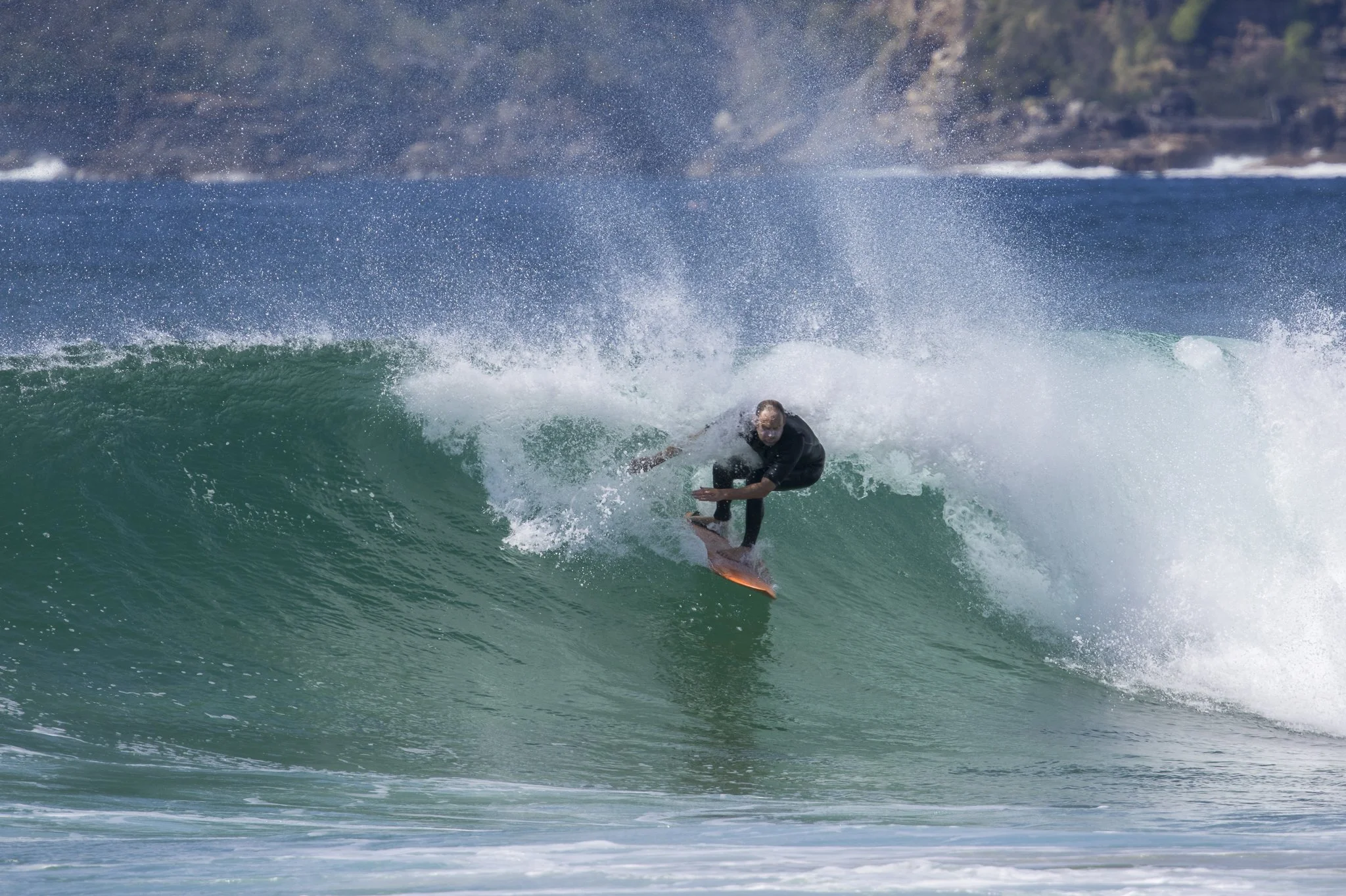 A person in a wetsuit surfing on a wave in the ocean with a rocky shoreline in the background.