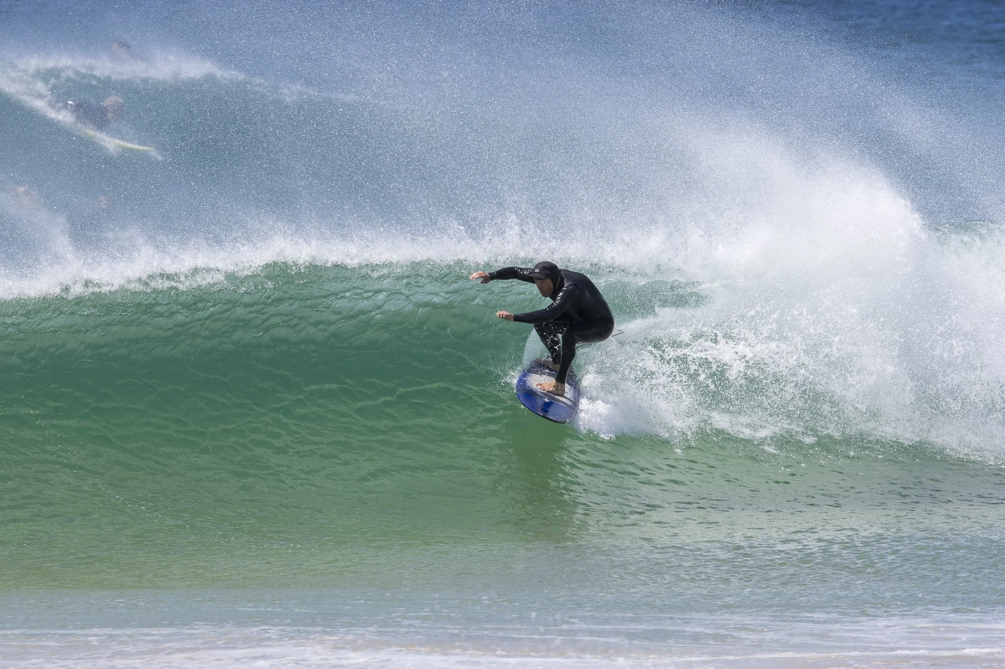 A person in black wetsuit riding a wave on a surfboard.