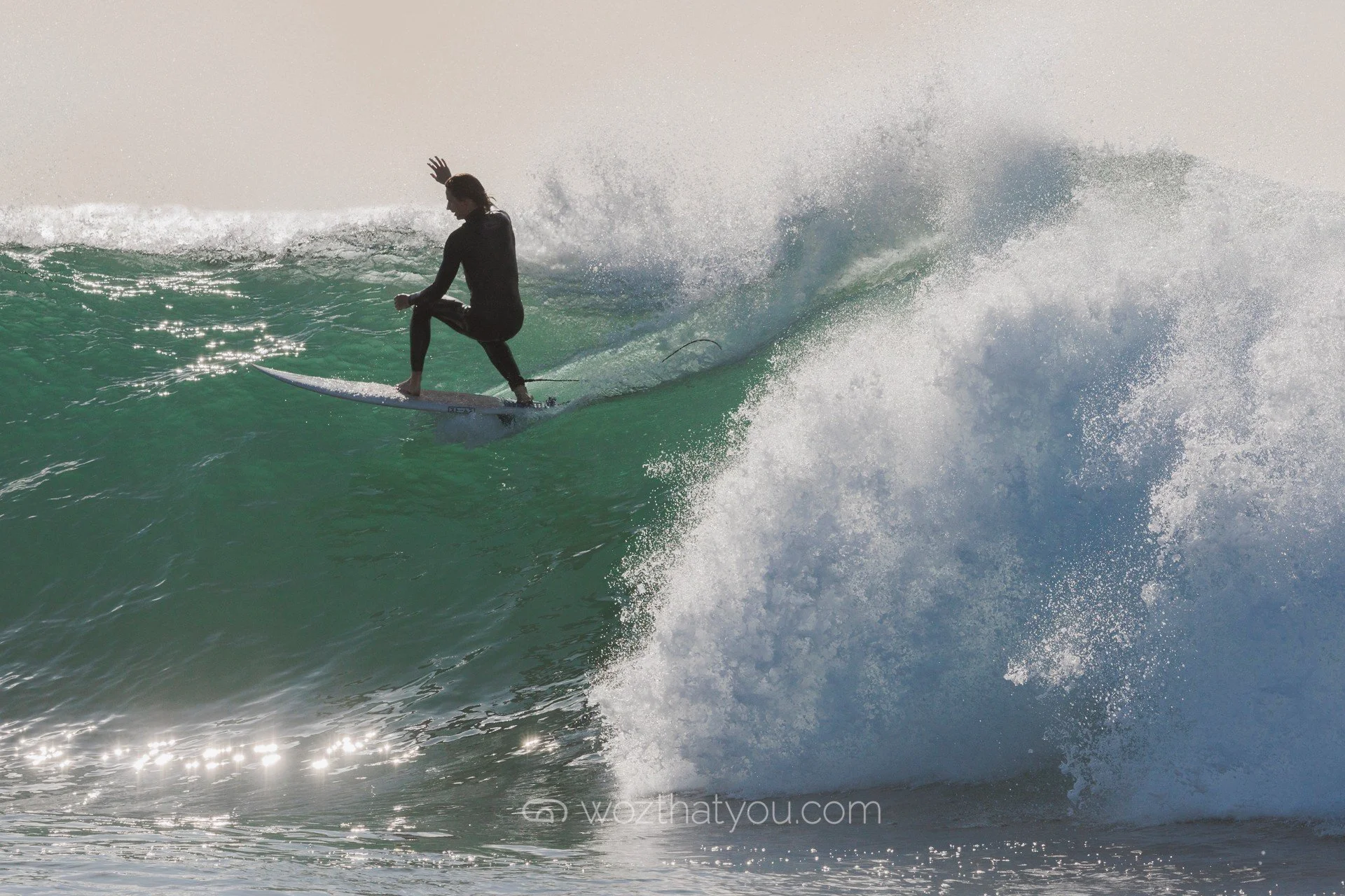 A person surfing on a wave in the ocean, wearing a black wetsuit.