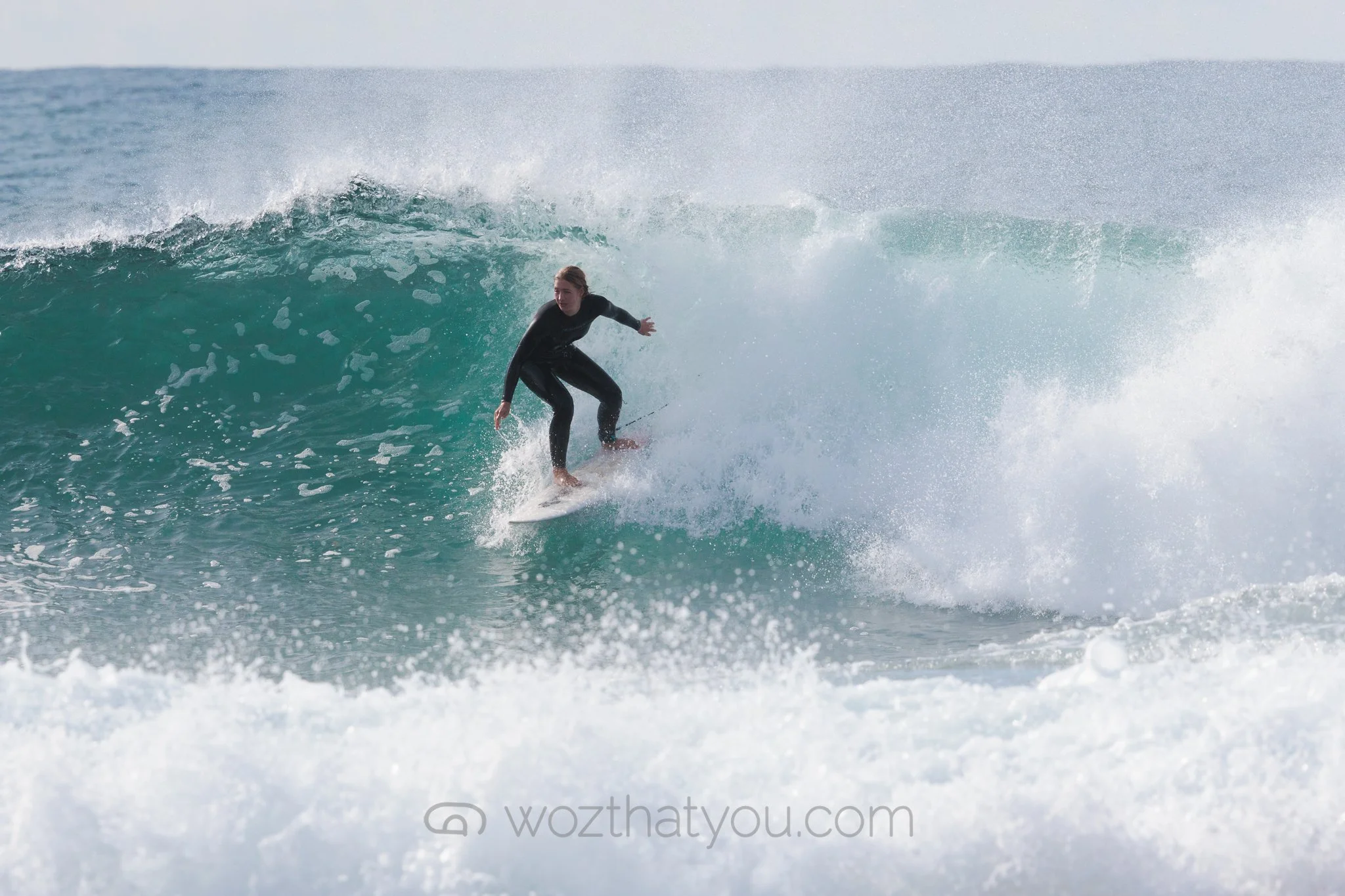 A woman surfing on a wave in the ocean while wearing a black wetsuit.