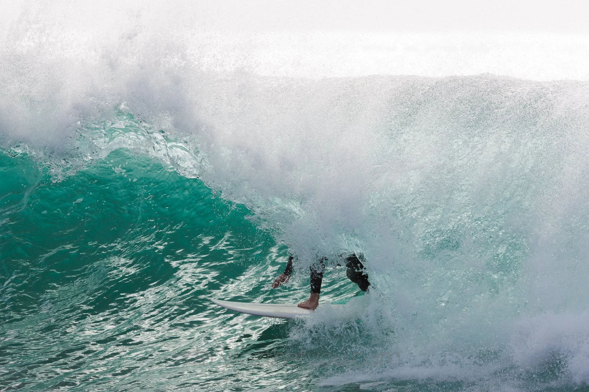 Surfer riding inside a large ocean wave, with the wave cresting overhead.