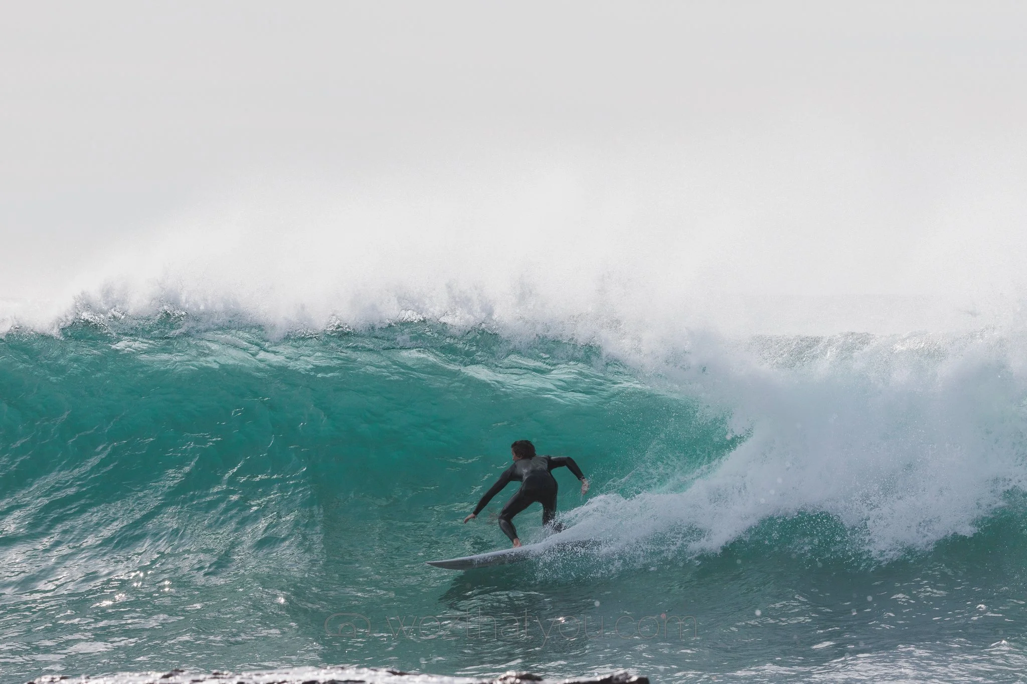 A person surfing on a large crashing wave in the ocean.