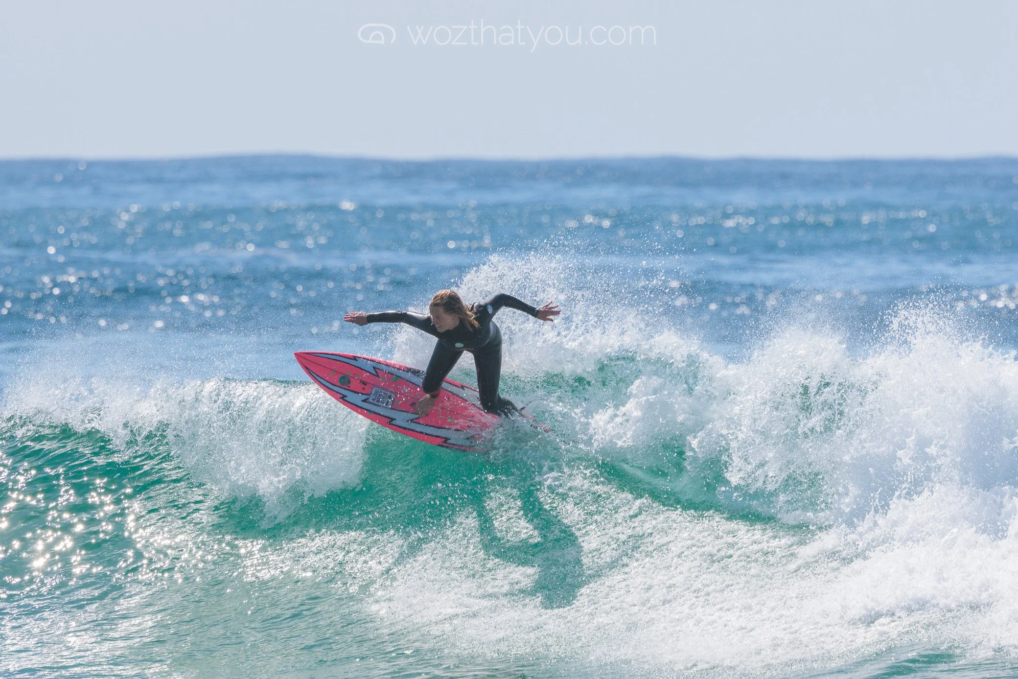 A woman surfing on a wave with a pink and blue surfboard in the ocean.