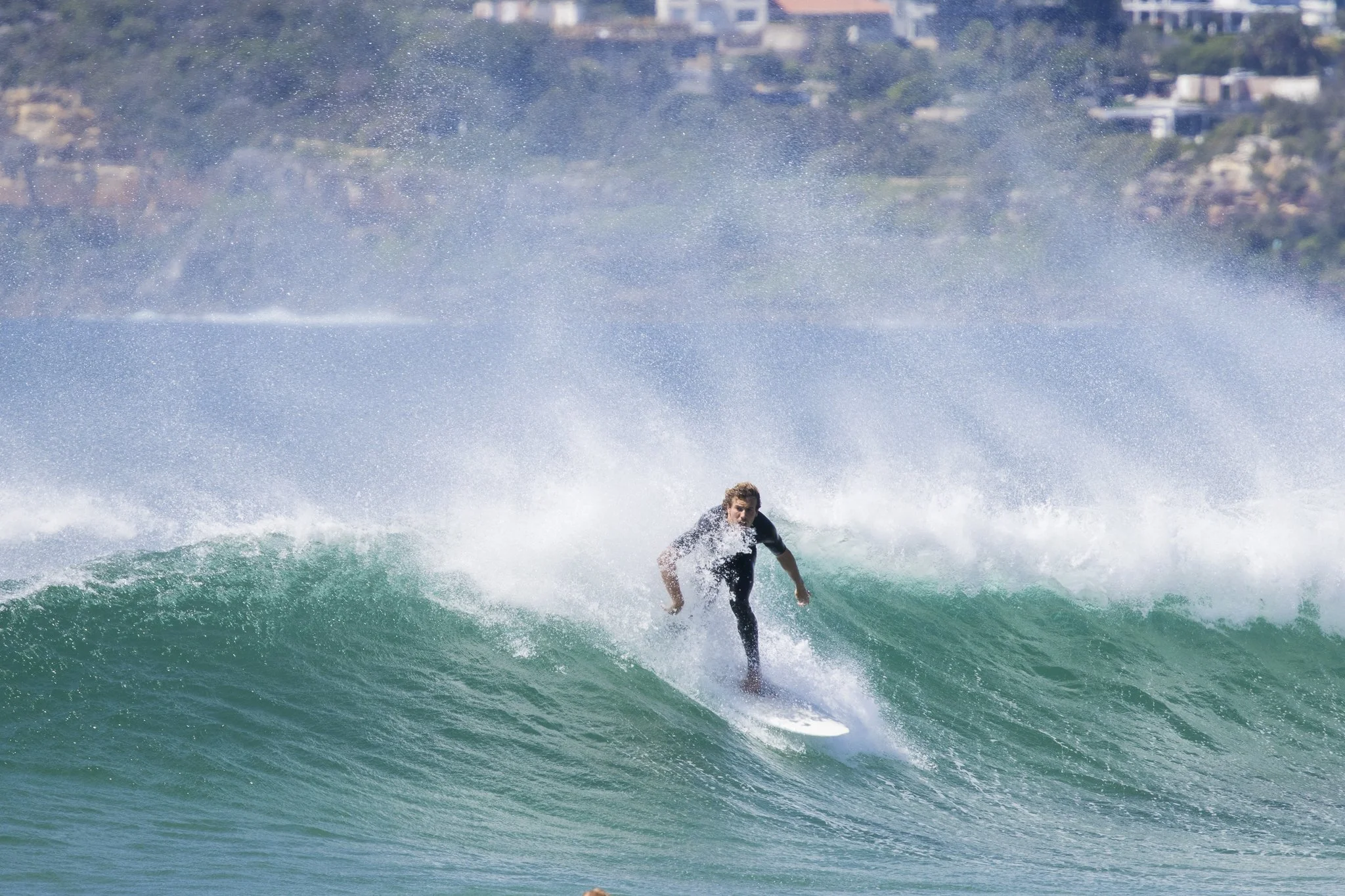 A person surfing on a wave in the ocean with a cityscape in the background.