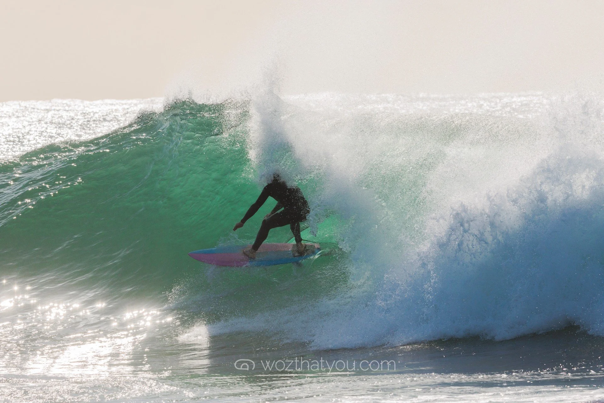 A person surfing on a wave at the beach during sunset.