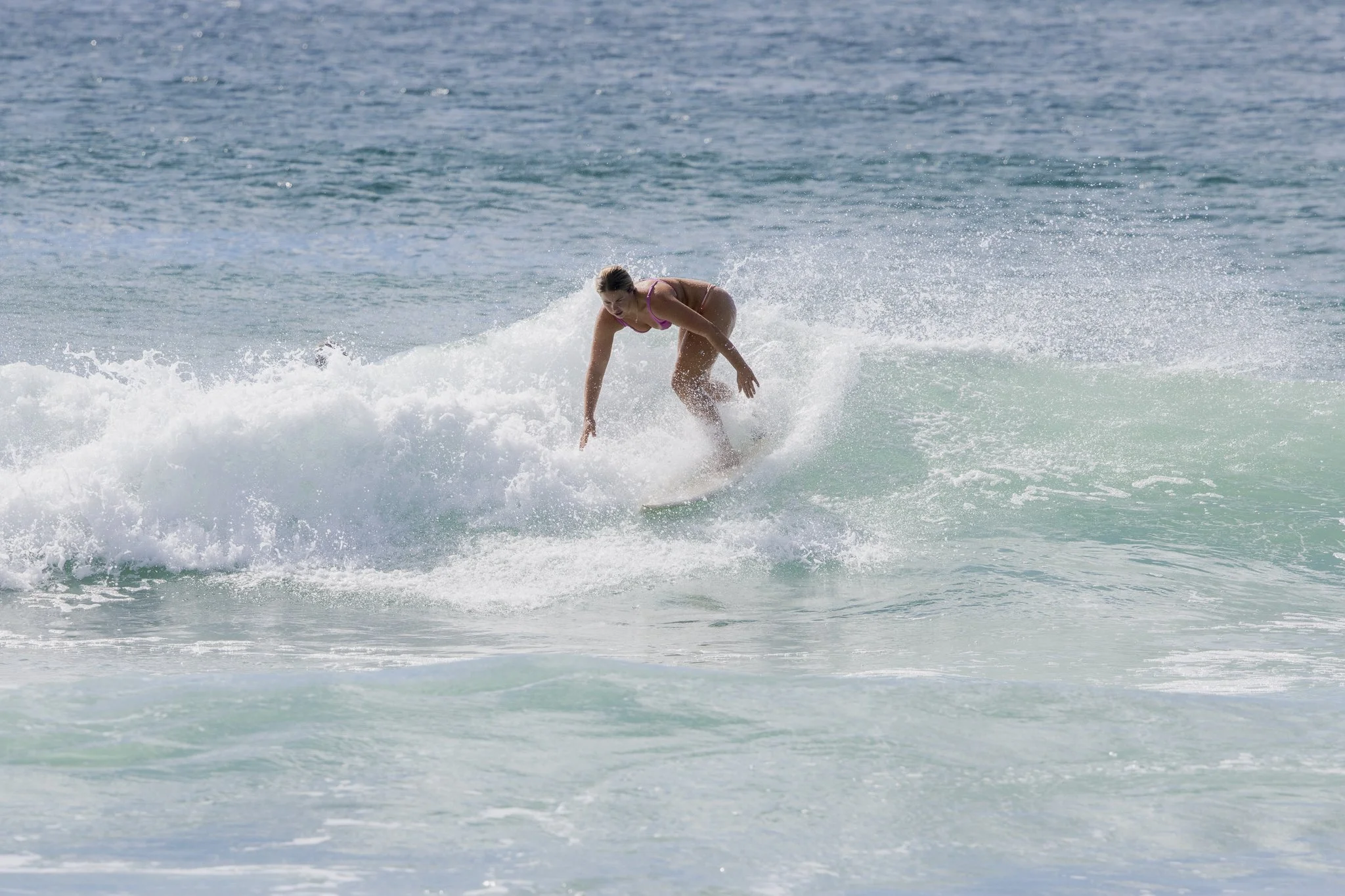 A woman surfing on a wave in the ocean, wearing a pink bikini.