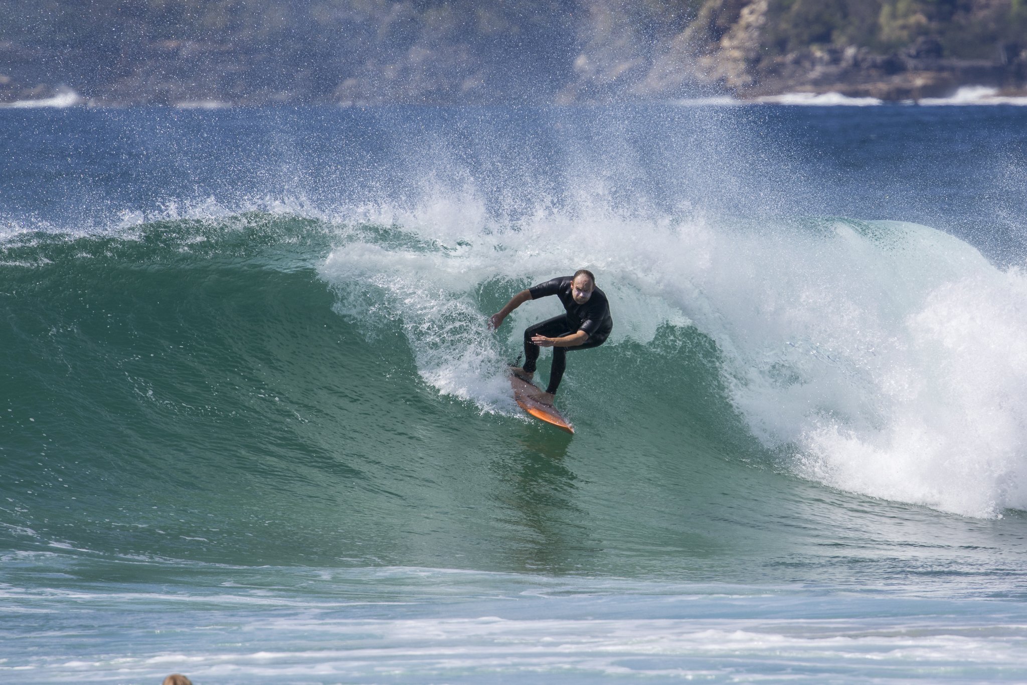 A person surfing a wave in the ocean with a rocky coastline in the background.