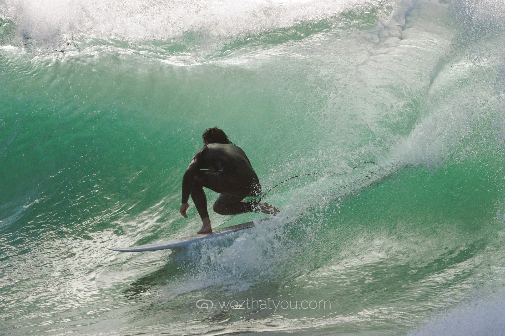 A person in black wetsuit surfing inside a large green wave.