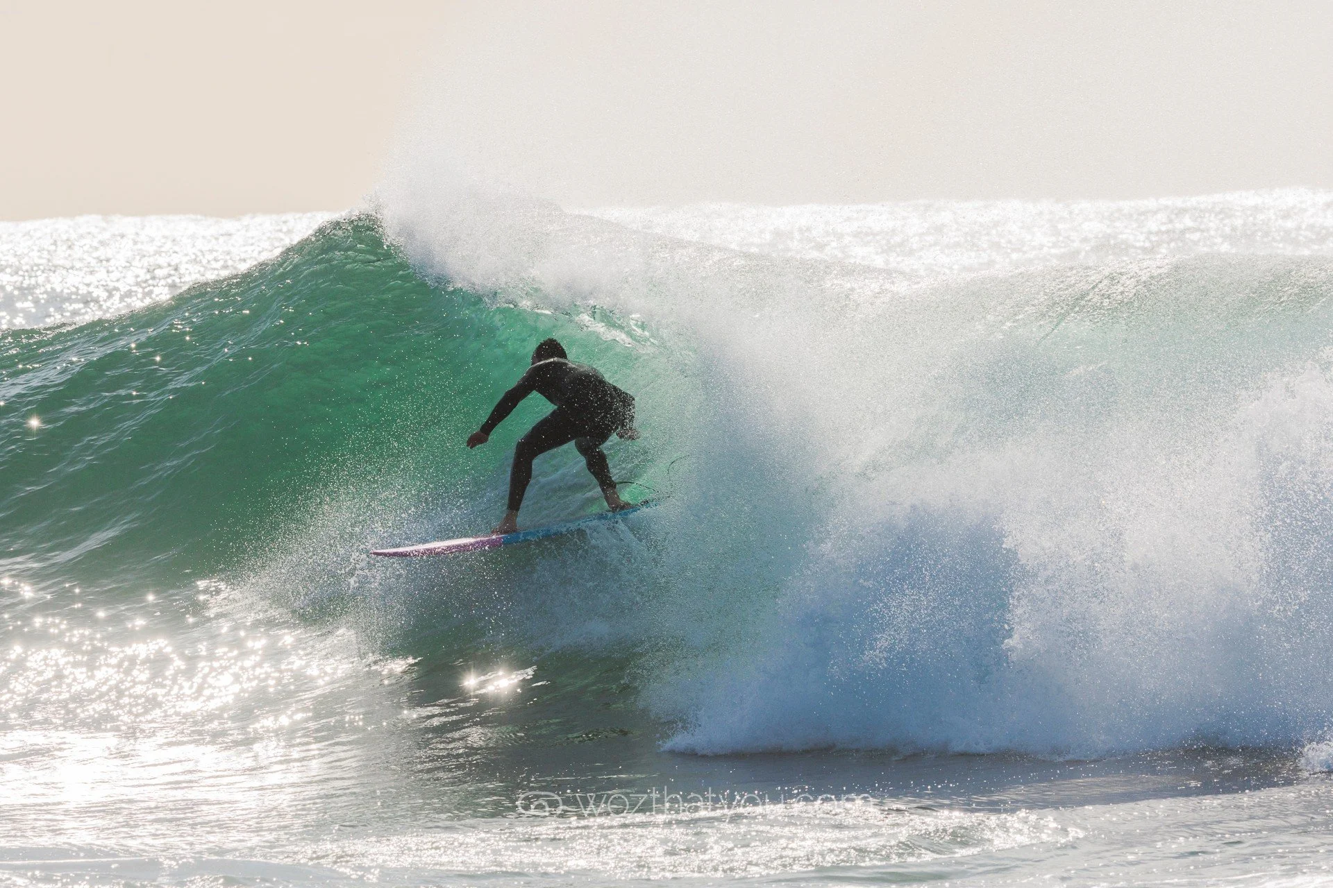 A person surfing on a large wave in the ocean with sunlight reflecting off the water.