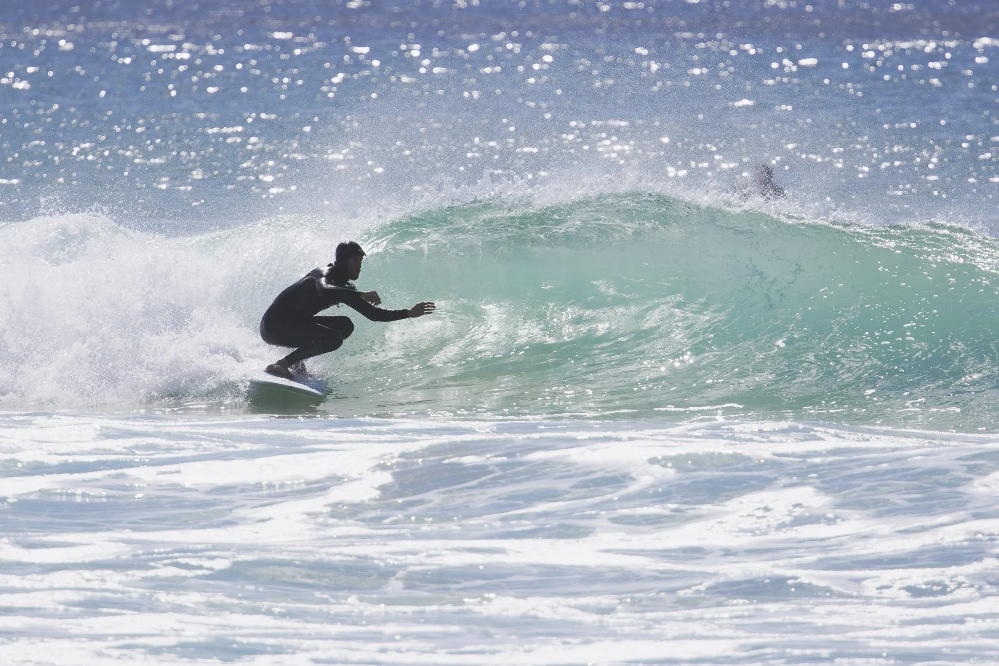 A person surfing on a wave in the ocean, wearing a black wetsuit.