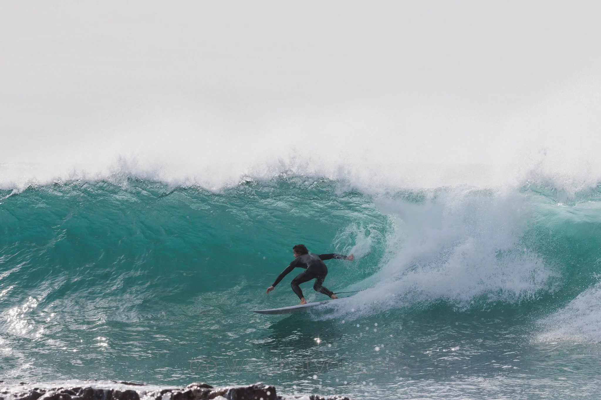 A person surfing on a large turquoise wave in the ocean.