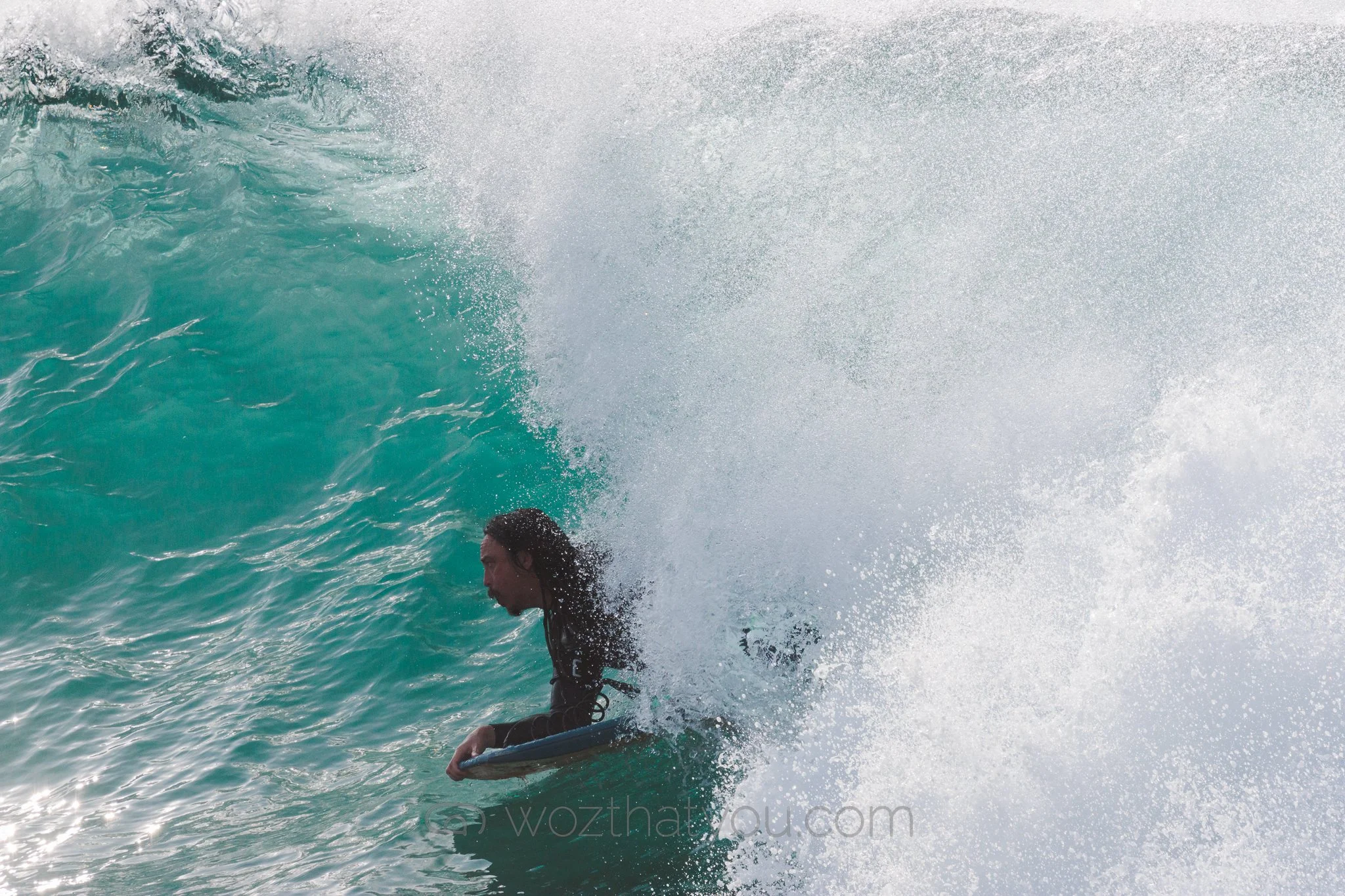 A person surfing on a large ocean wave with white spray.