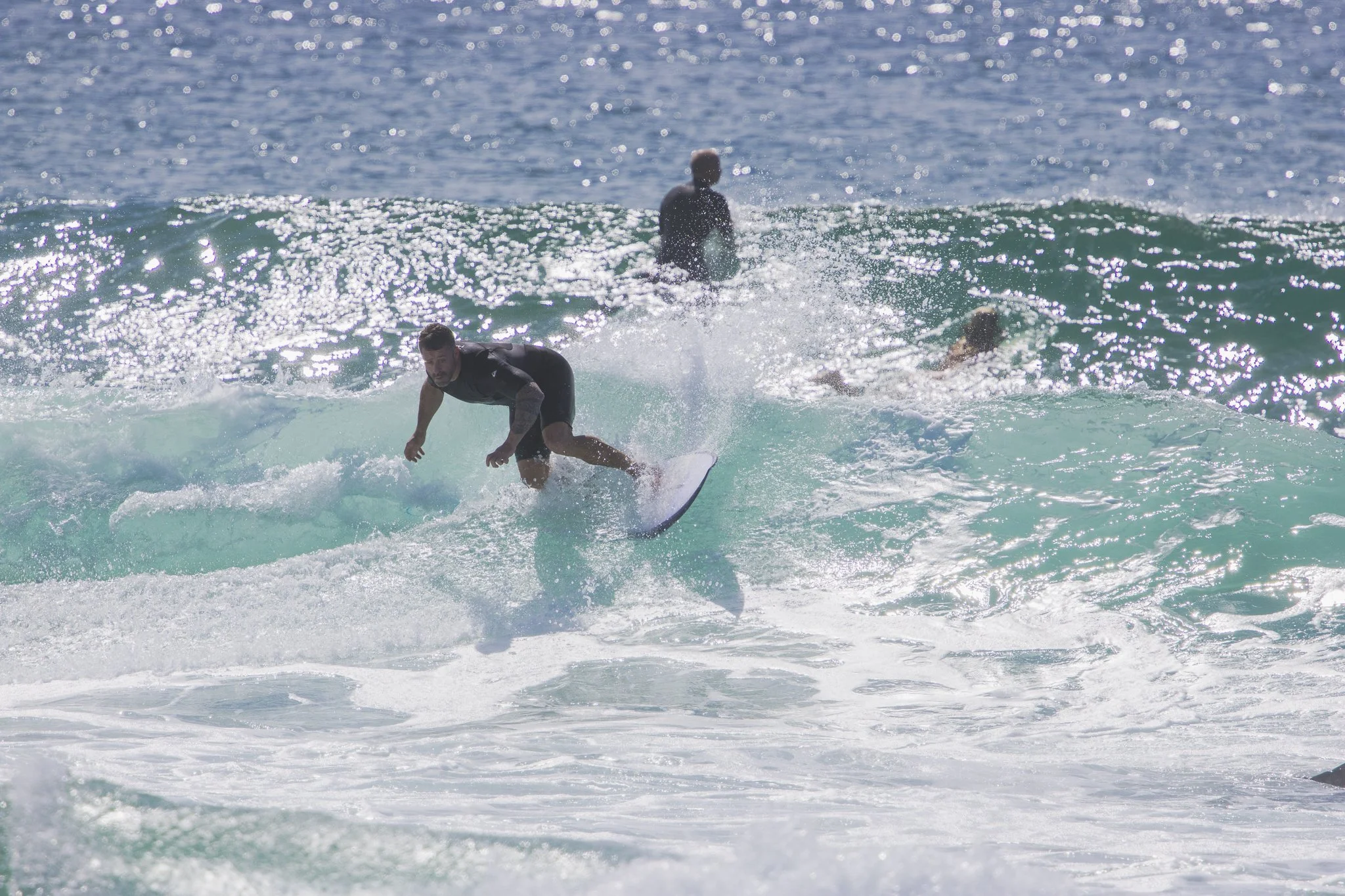 A person surfing on a wave in the ocean with two other surfers in the background.