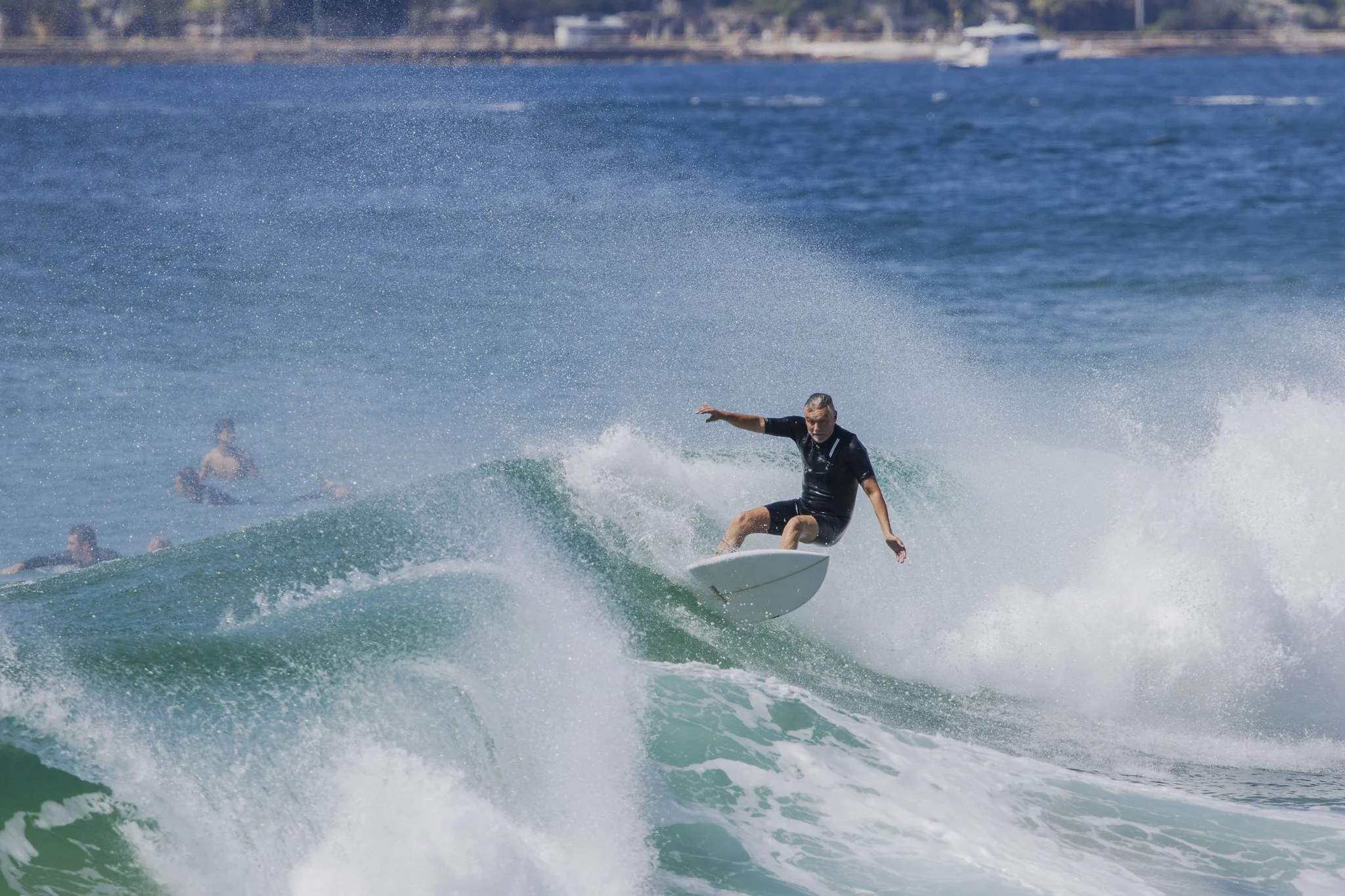 A man surfing on a wave in the ocean with other surfers in the background.