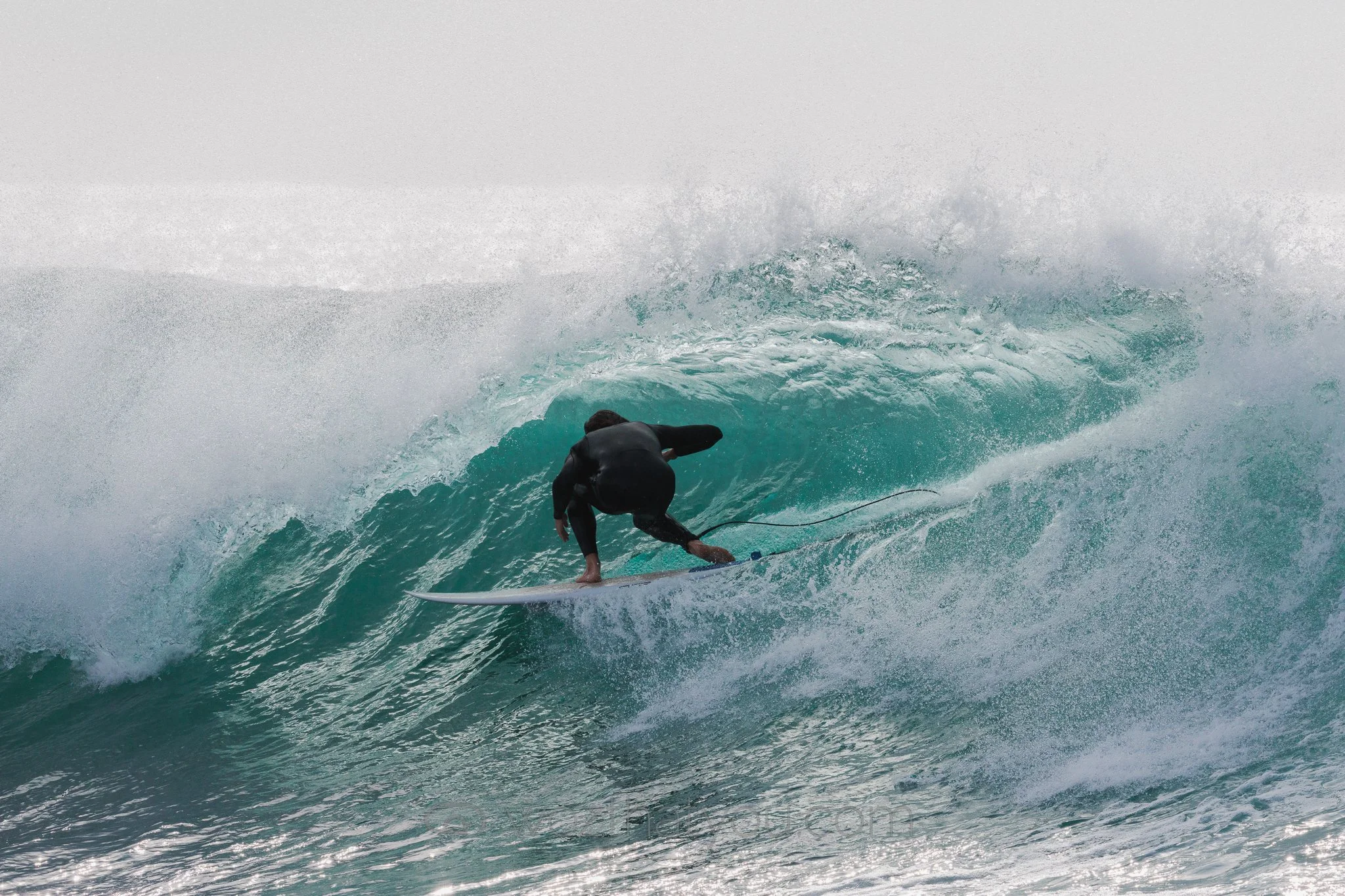 Surfer in black wetsuit riding a turquoise wave on a surfboard.