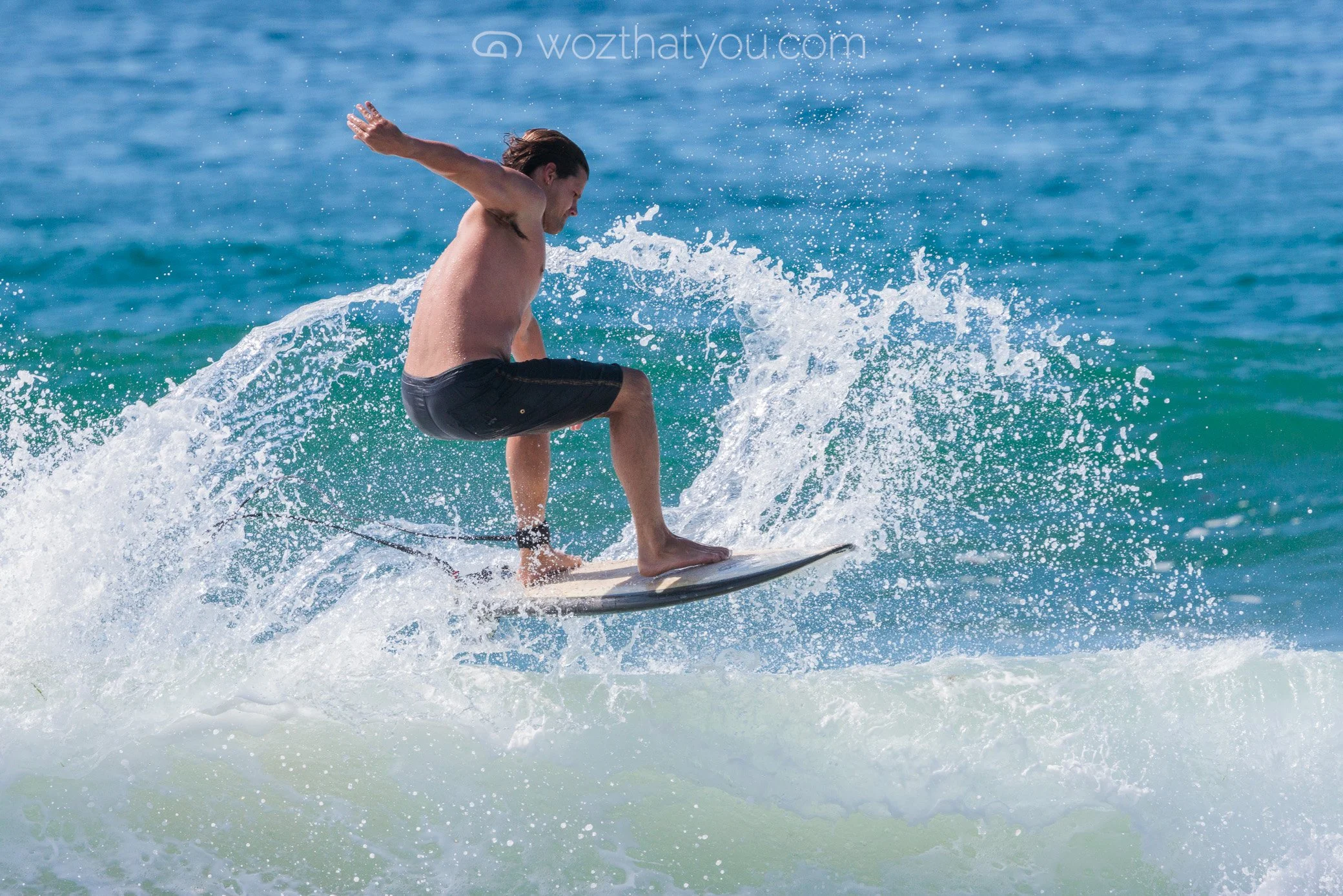 A man with long hair surfing on a wave in the ocean.