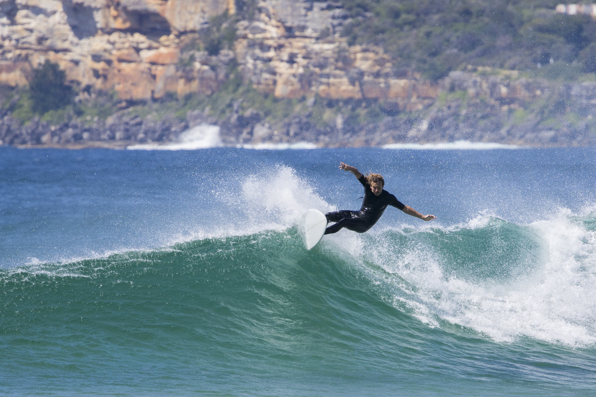A person surfing on a wave in the ocean with cliffs in the background.