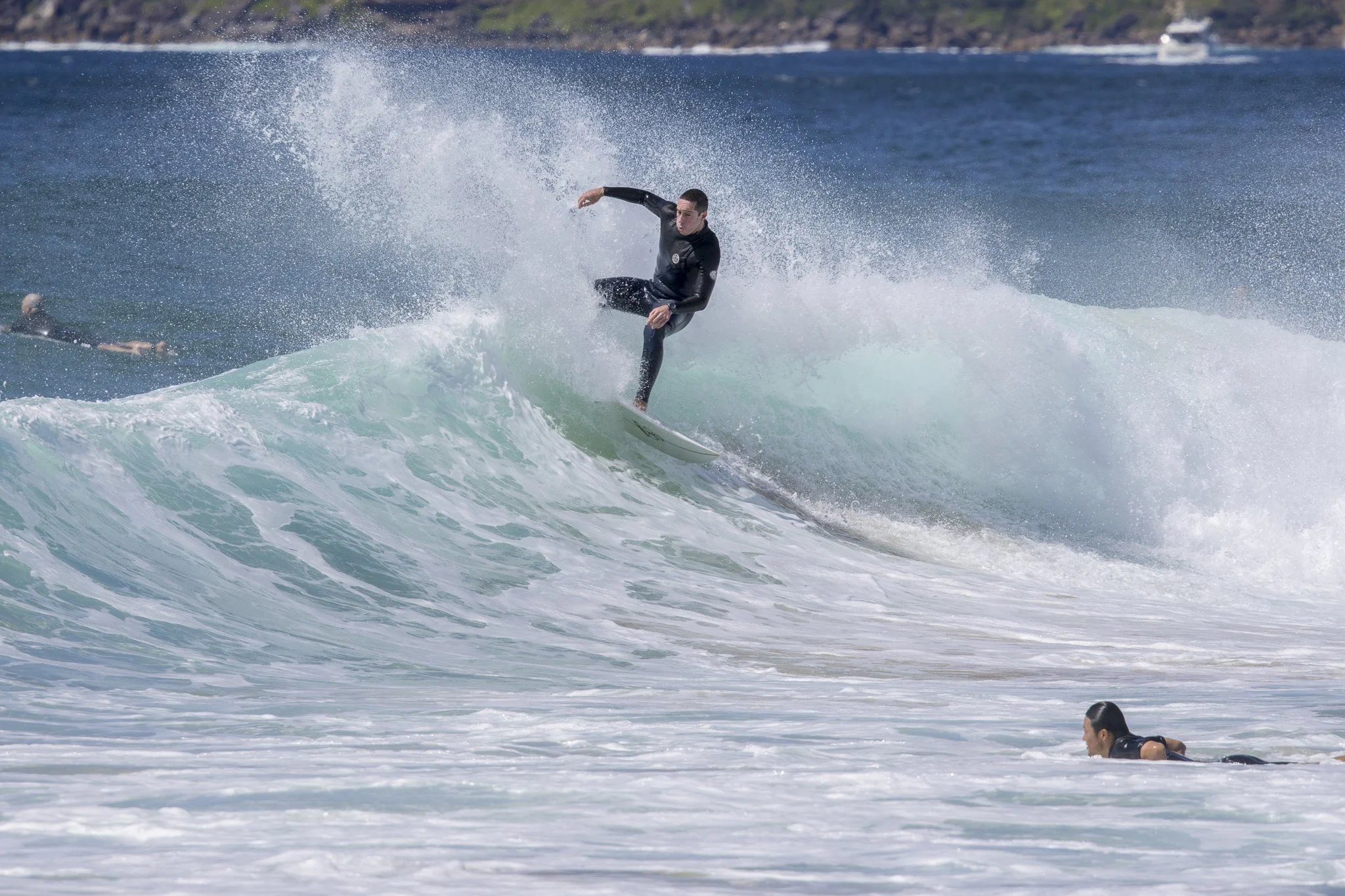 A person surfing on a wave in the ocean with another person swimming nearby.