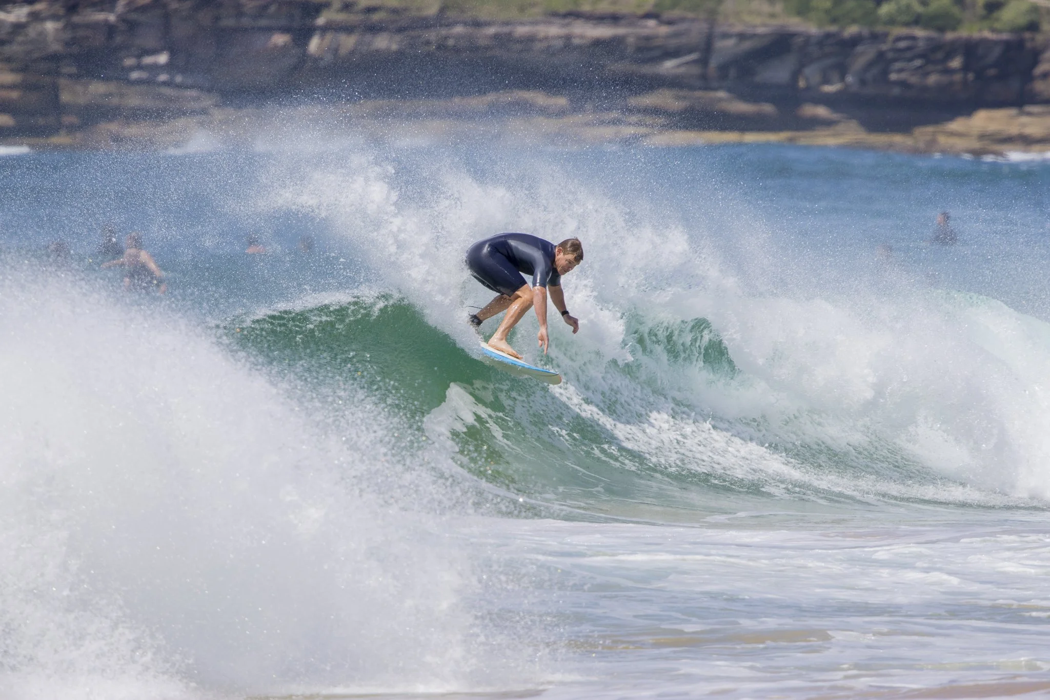 A man in a wetsuit surfing a wave at a beach with rocky cliffs in the background.