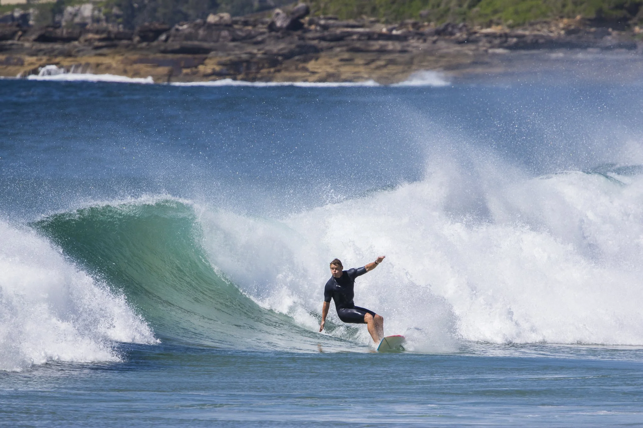 A man surfing on a wave in the ocean near a rocky shoreline.