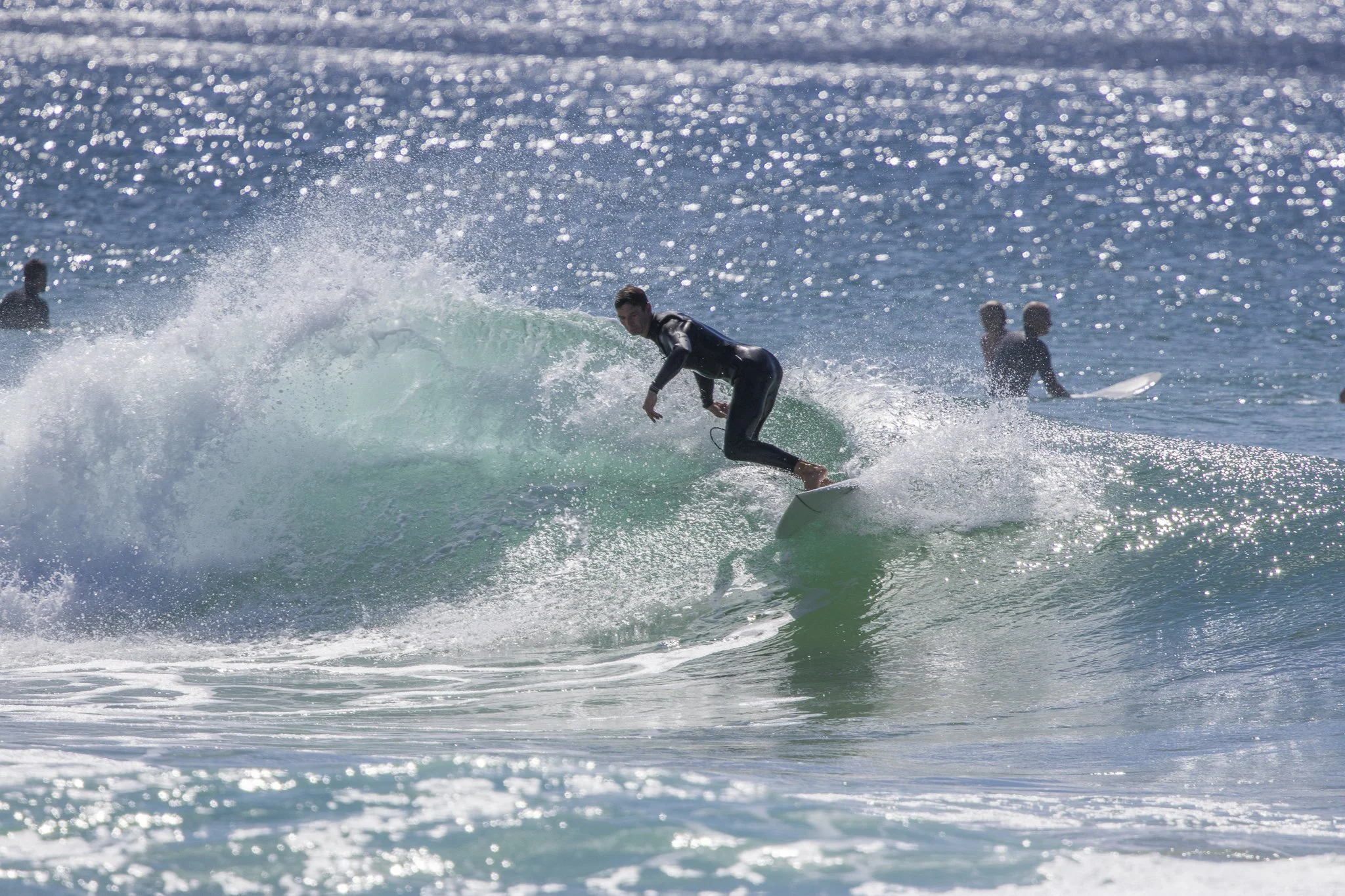 A person in a wetsuit surfing on a wave at the beach with other surfers in the background.