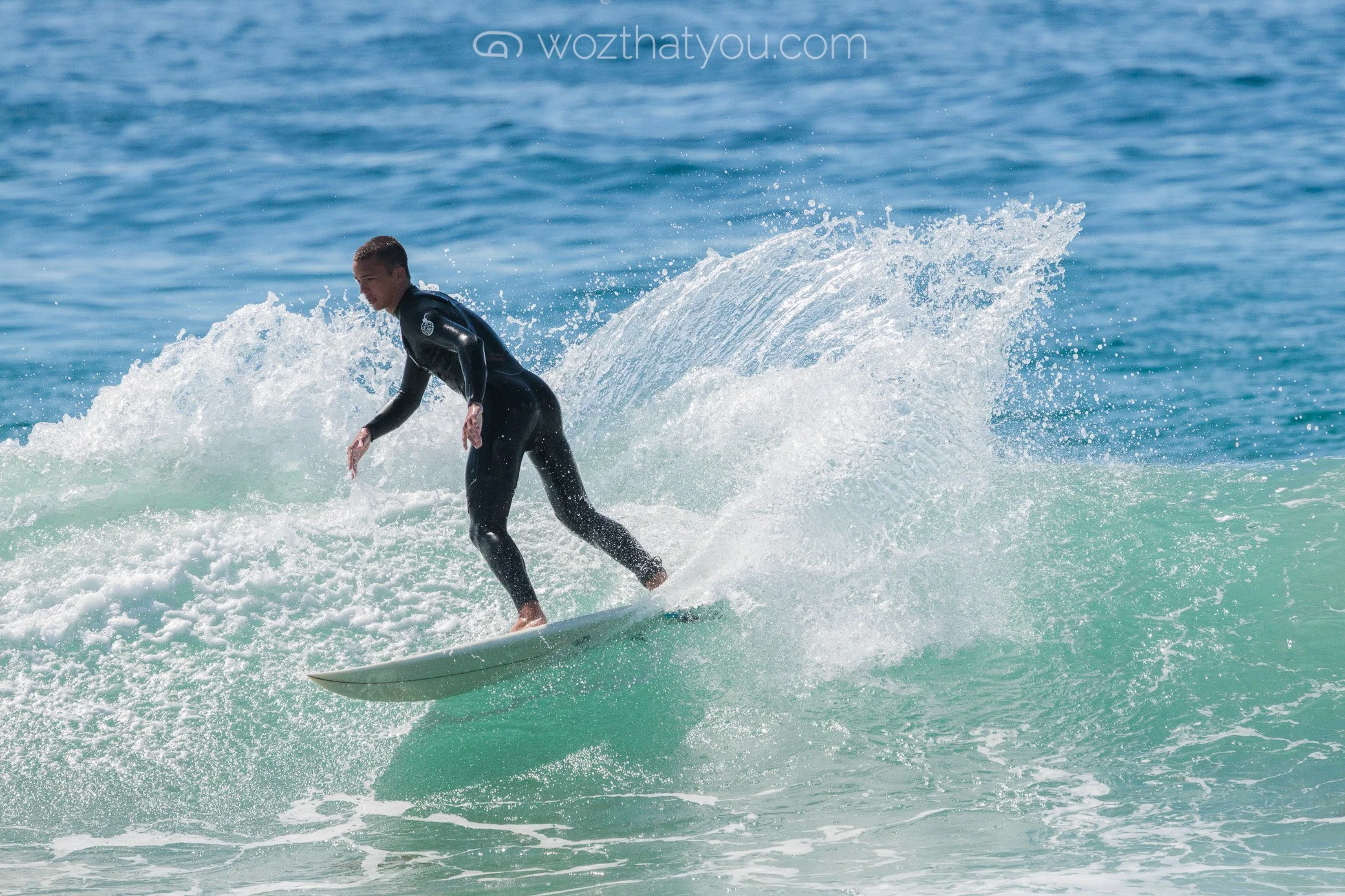 A person in a black wetsuit surfing on a small wave in the ocean.