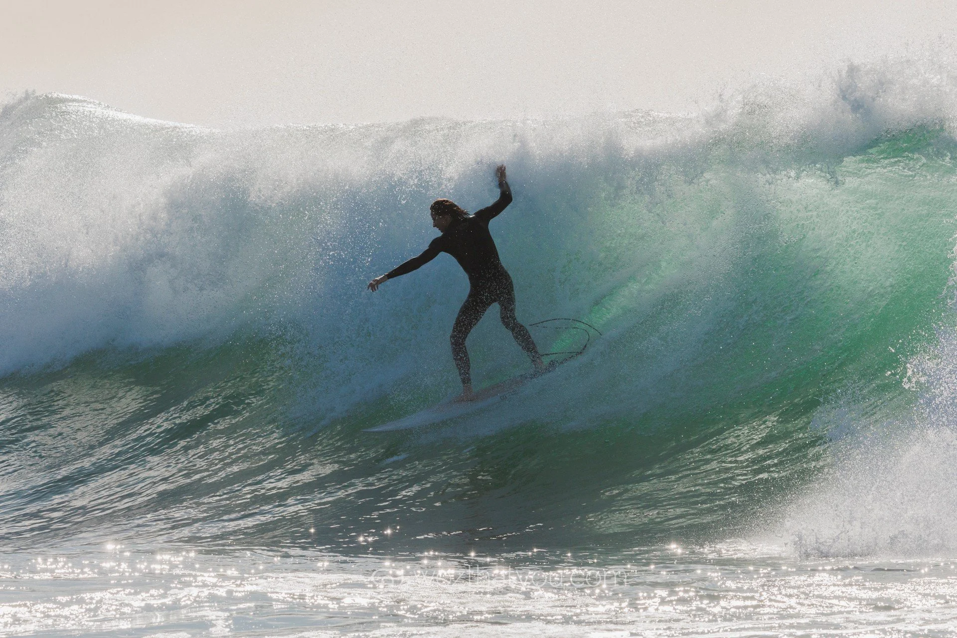 A surfer dressed in black riding a large wave in the ocean.