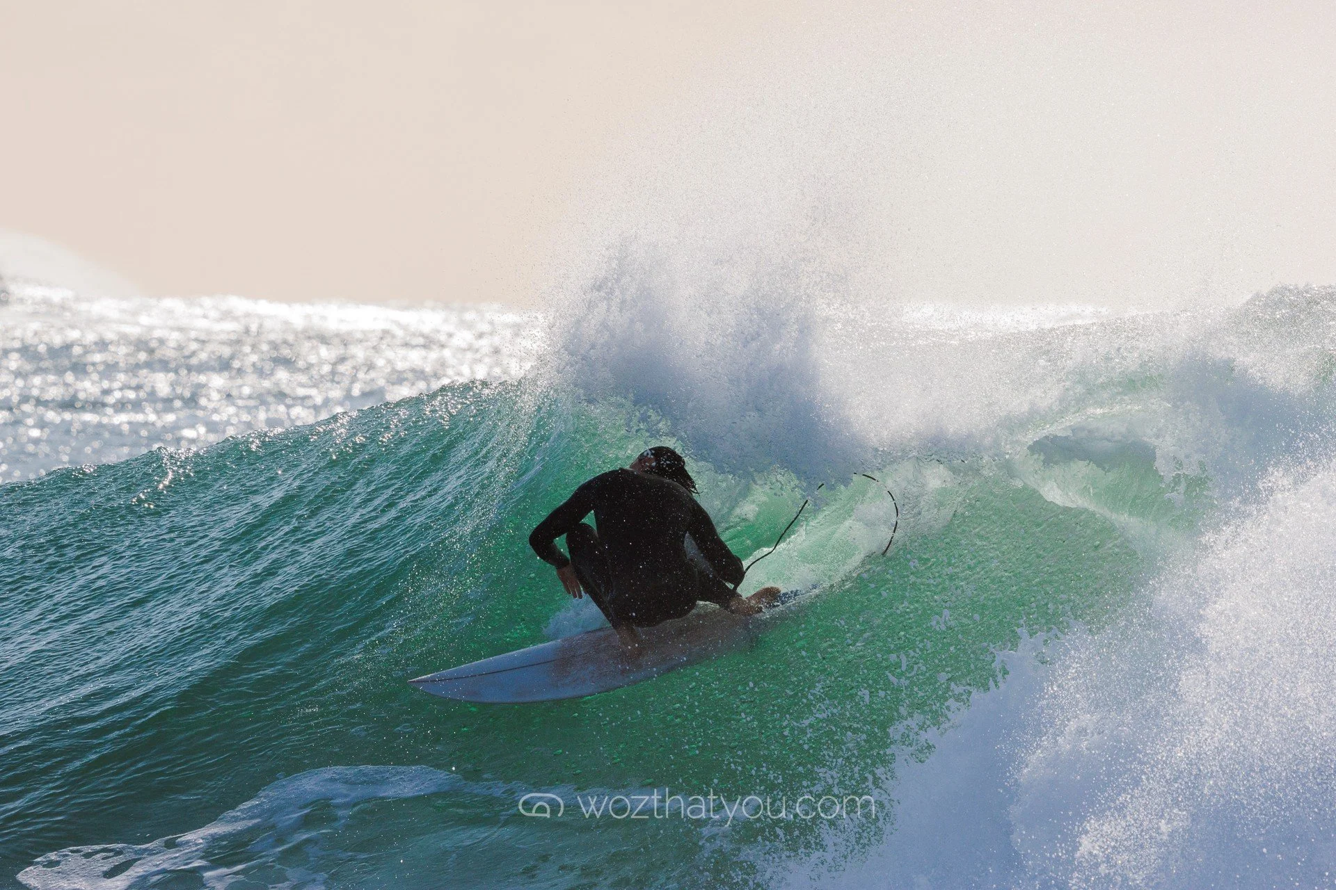 A person in black wetsuit riding a surfboard on a large green wave.