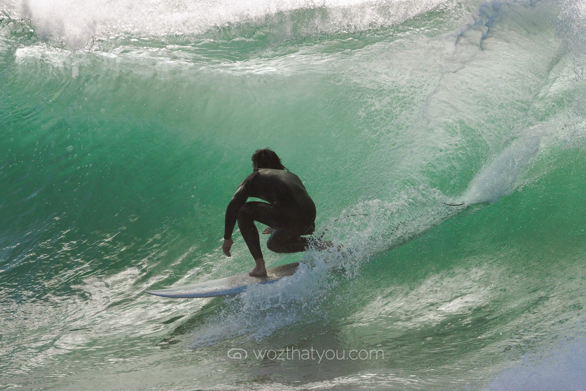 A person wearing a black wetsuit riding a surfboard inside a large green wave.