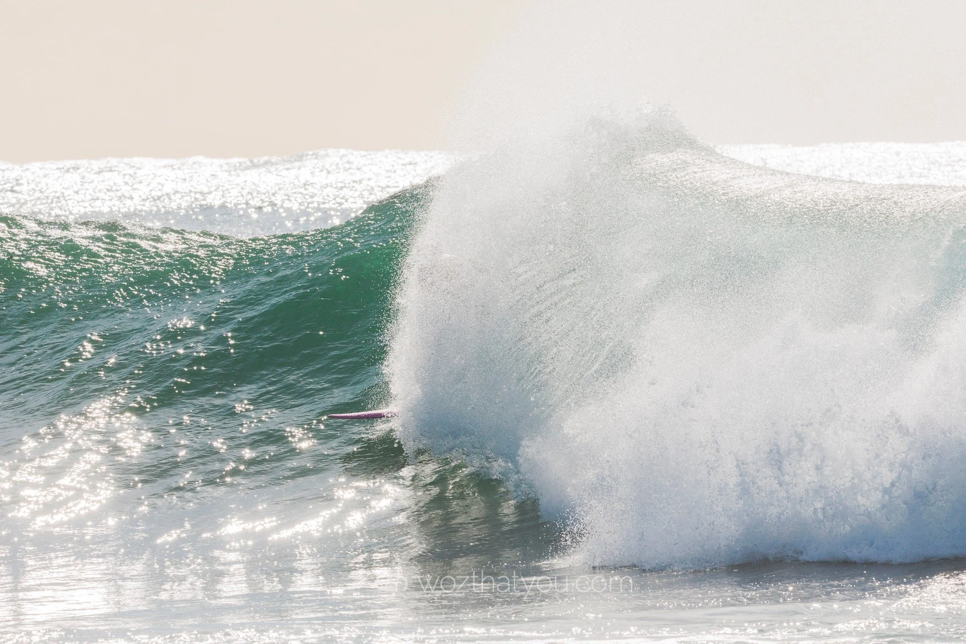 A surfer riding a large wave crashing in the ocean, with sunlight reflecting on the water.