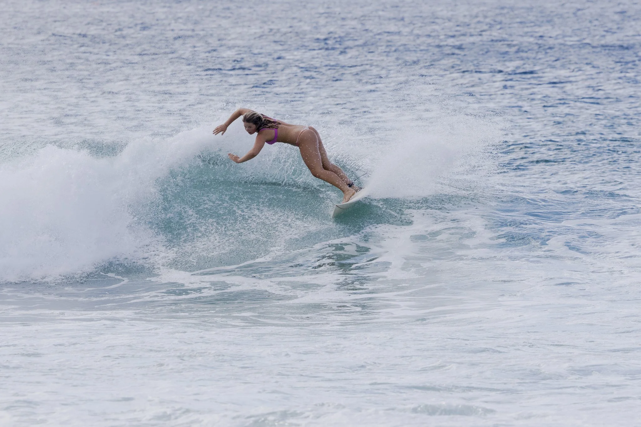 A woman surfing on a wave in the ocean, wearing a pink bikini.