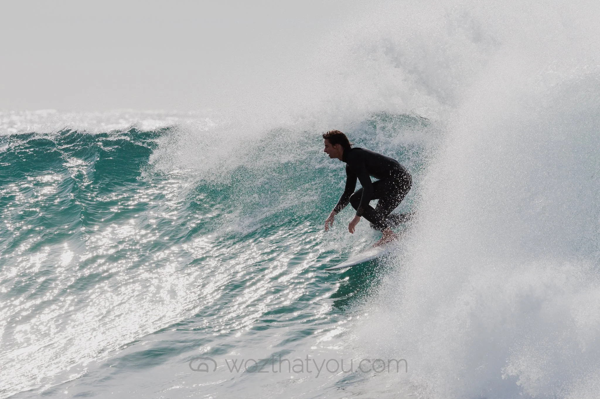 A man surfing on a wave in the ocean, wearing a black wetsuit.