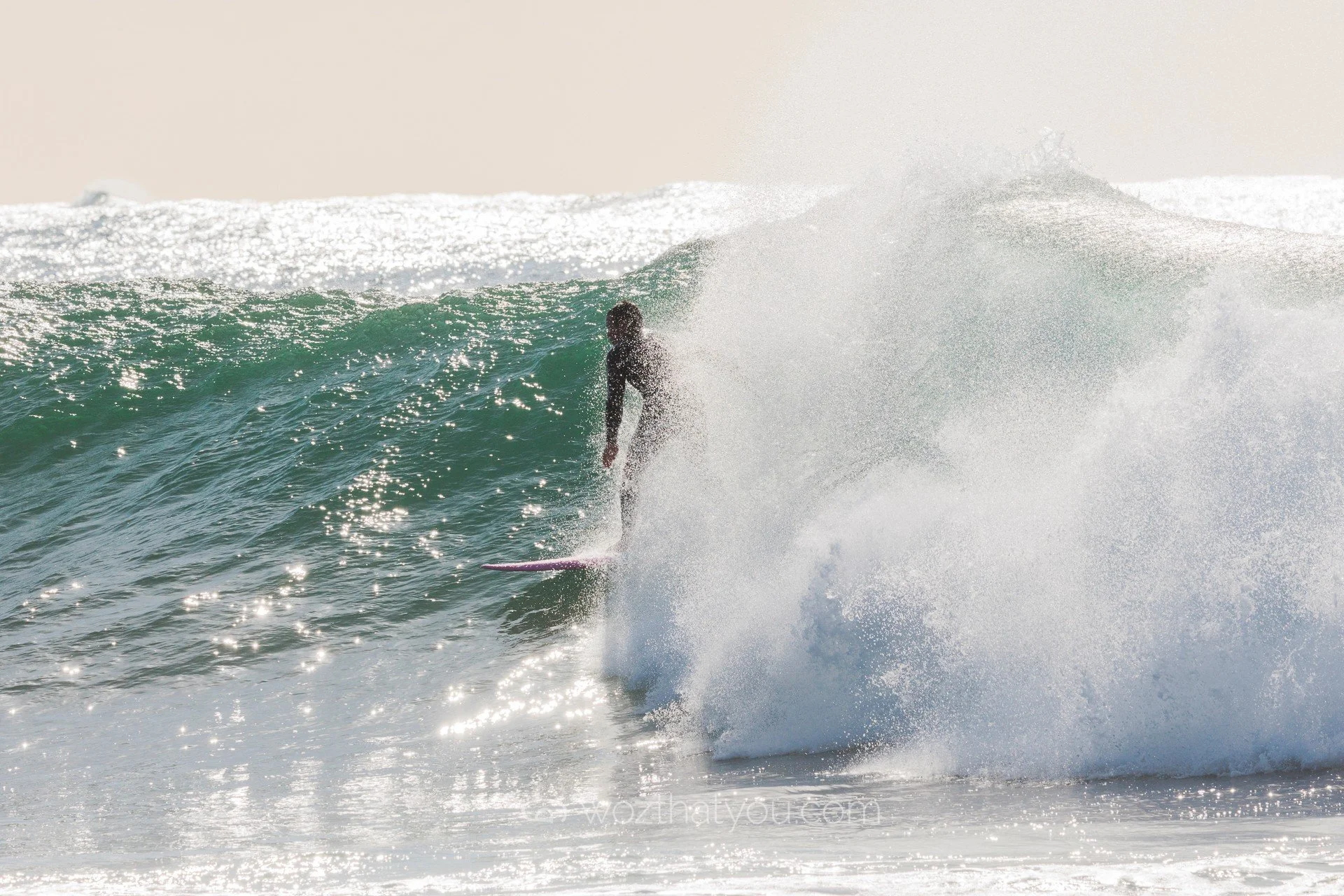 A person surfing a wave in the ocean with sunlight reflecting off the water.
