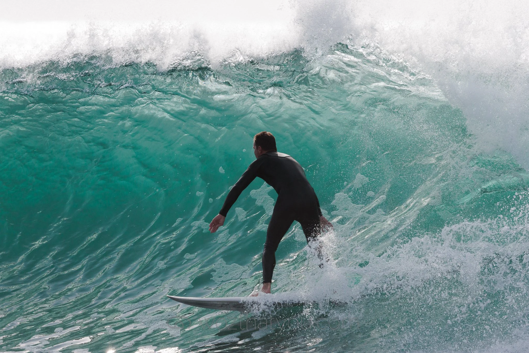 A man in a black wetsuit surfing on a large ocean wave.