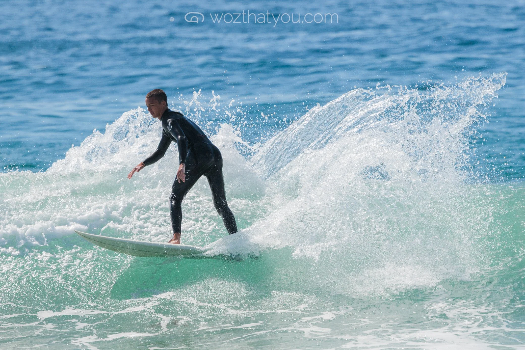A person surfing on a wave in the ocean, wearing a black wetsuit.