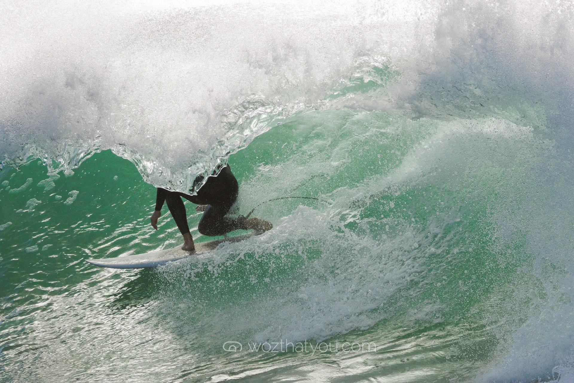 A surfer riding inside a green ocean wave wearing a black wetsuit