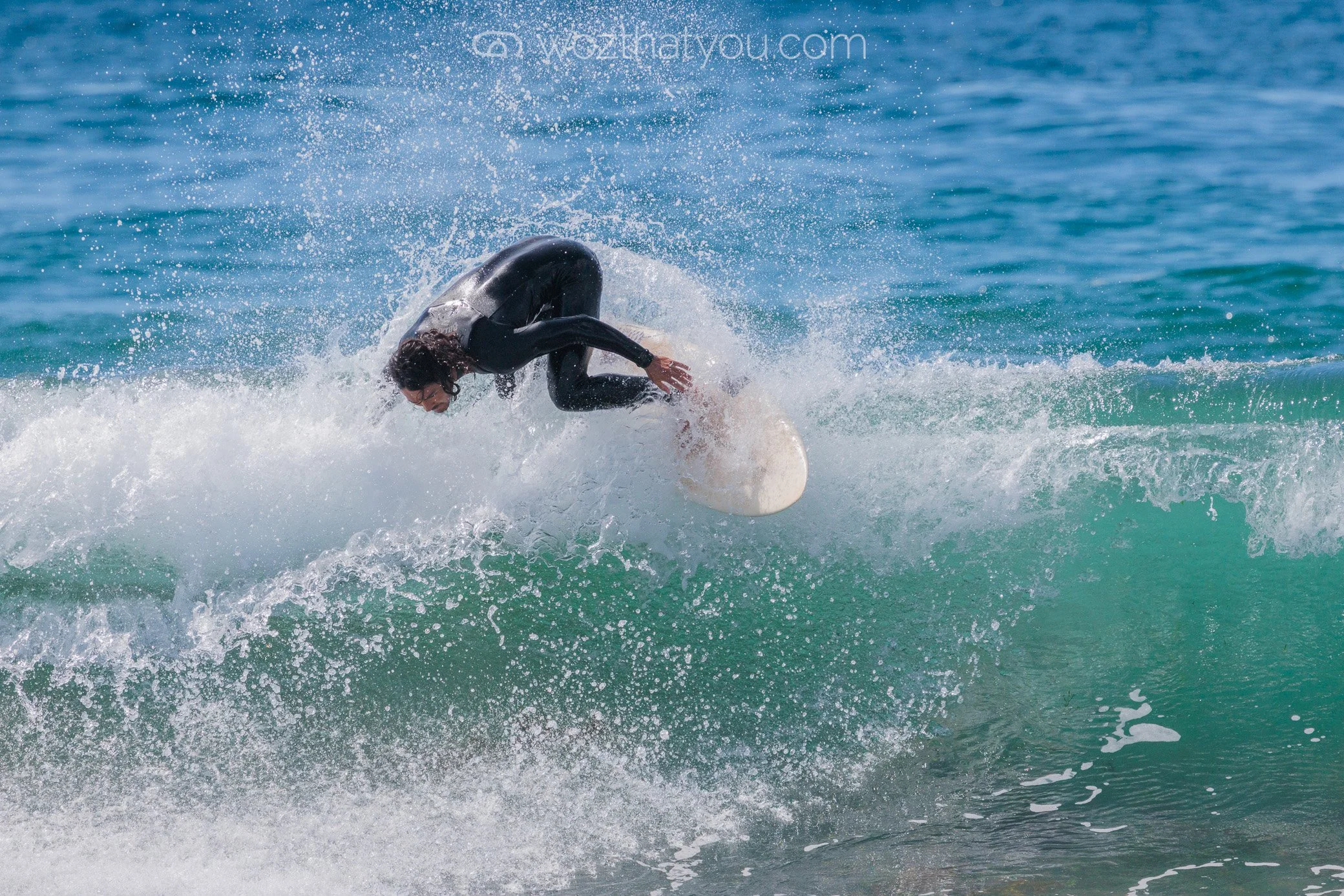 Person surfing on a wave in the ocean, wearing a black wetsuit.