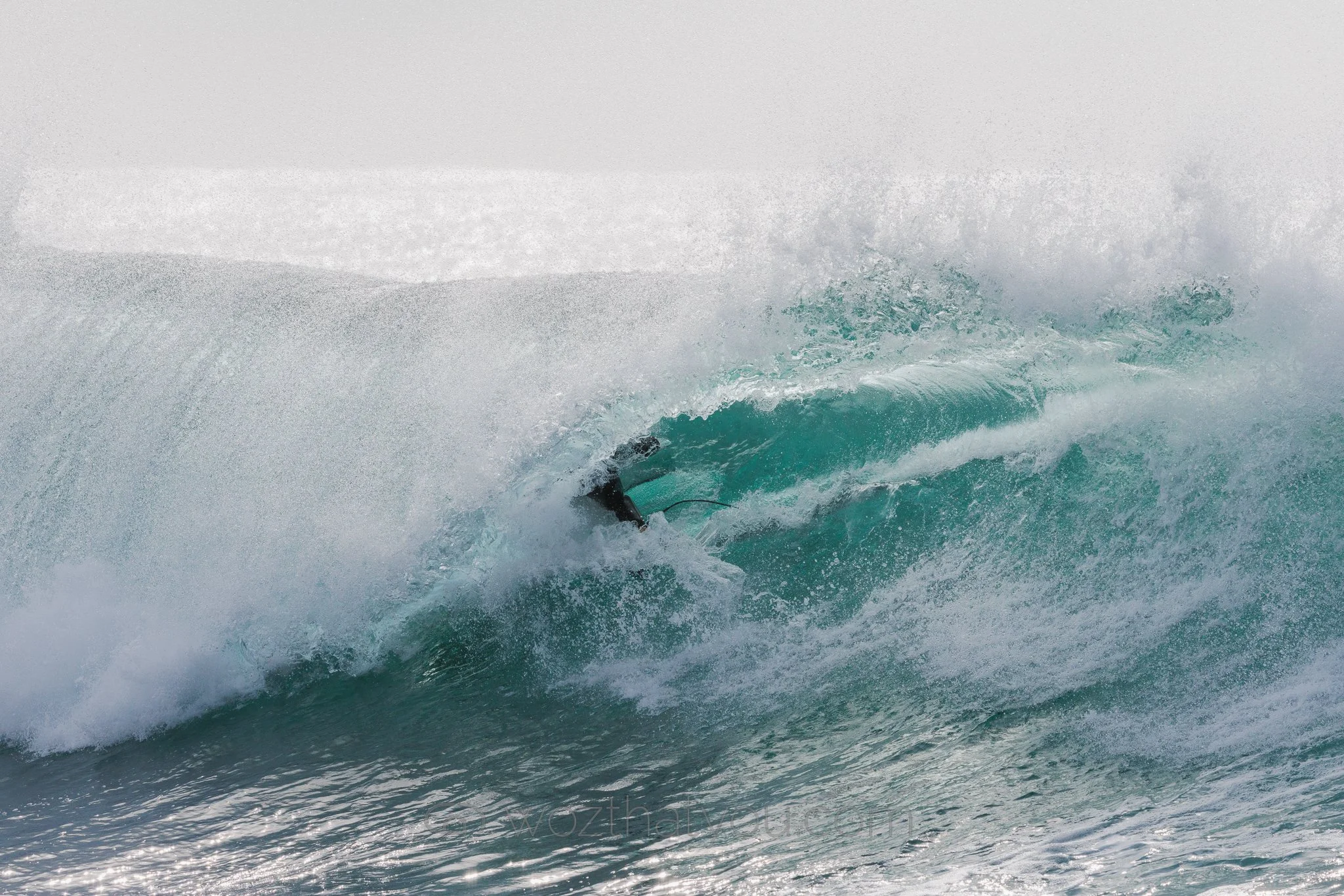 A surfer riding inside a large ocean wave during the daytime.