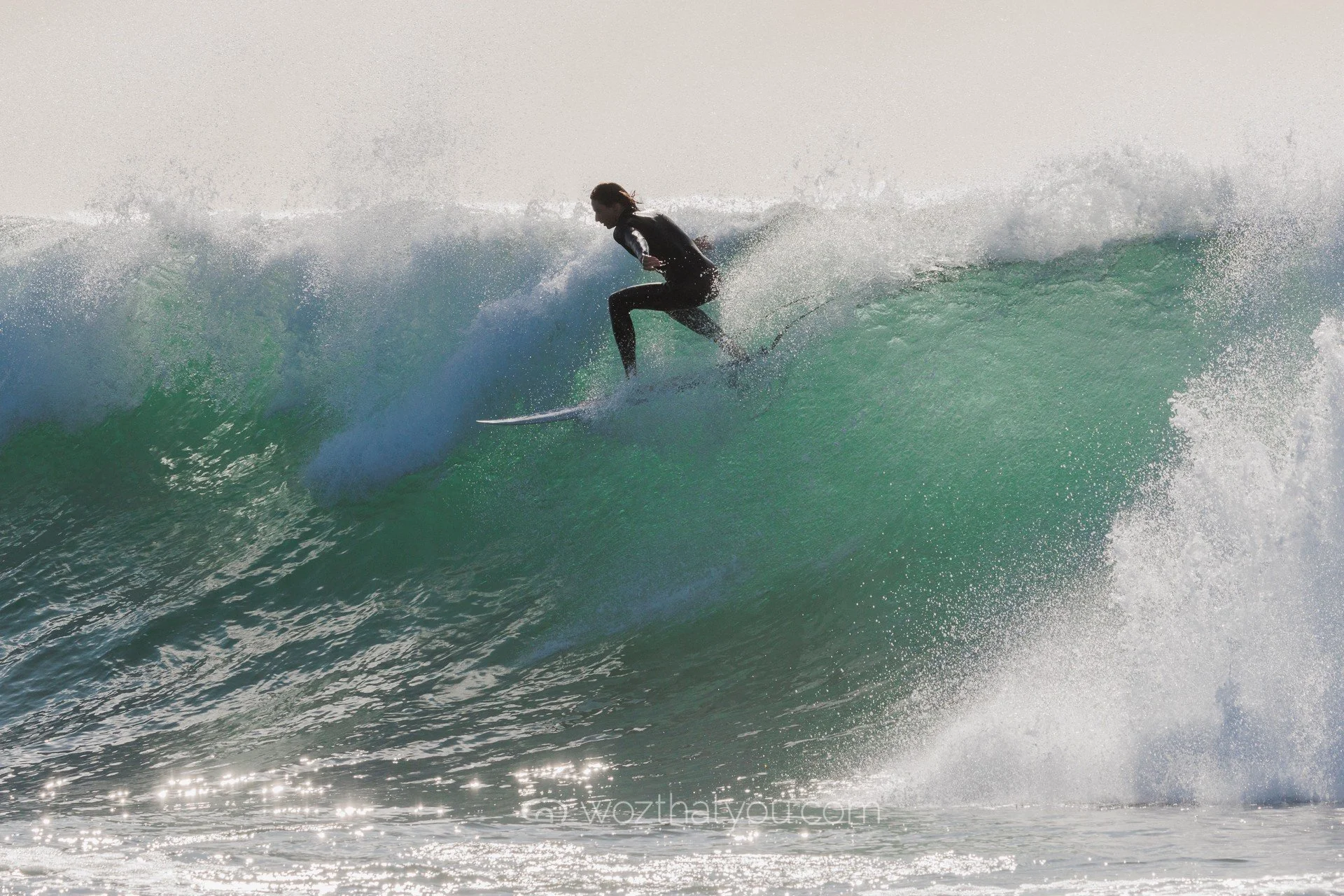 A person surfing on a large green wave in the ocean during daylight.