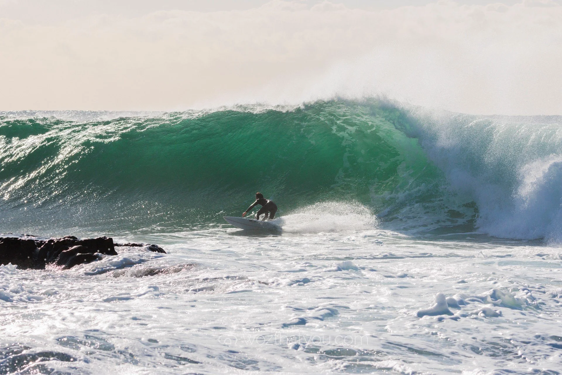 A surfer riding a large green wave in the ocean, with foam and spray around.