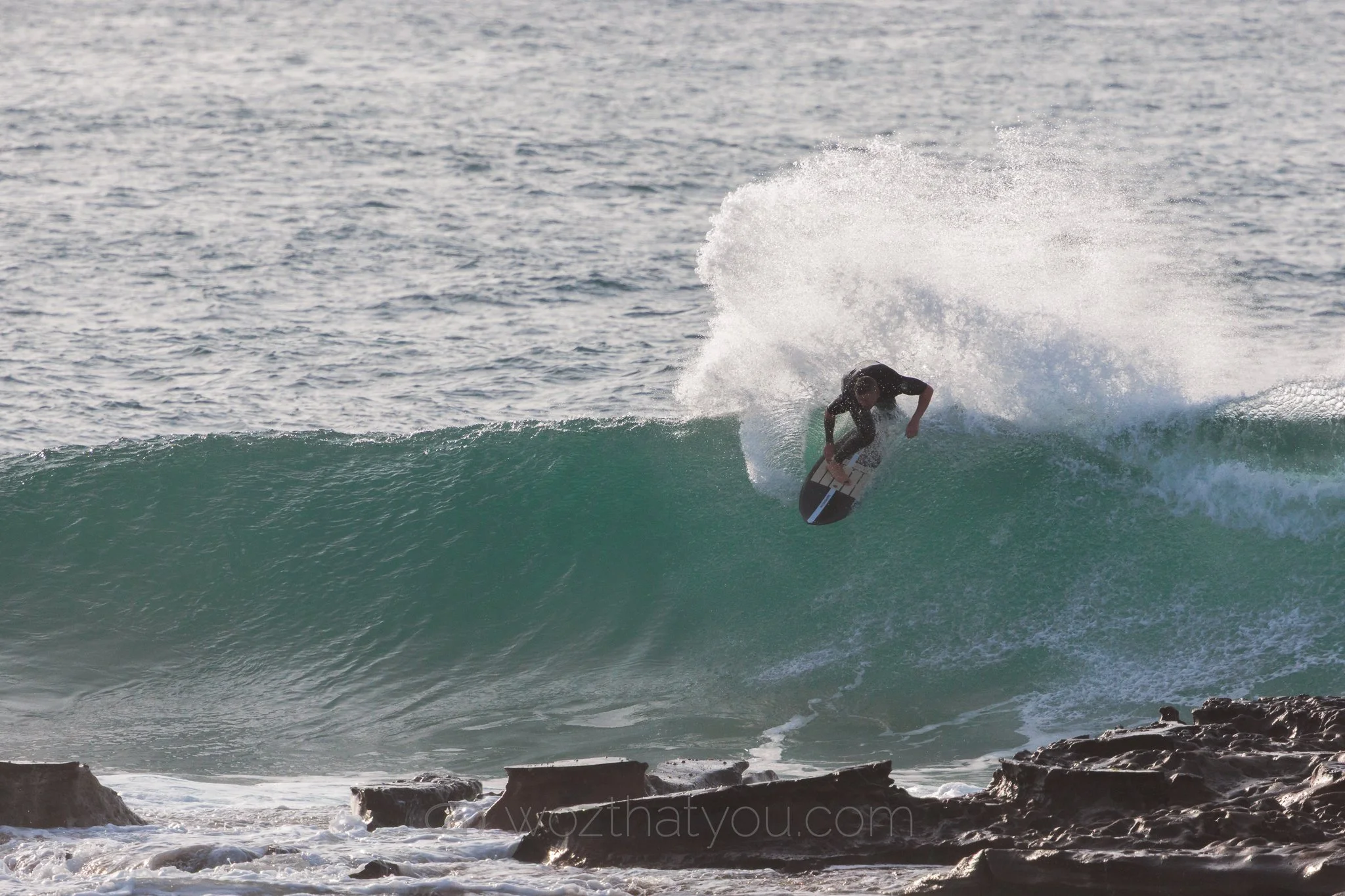 A person surfing on a wave near rocky shoreline.