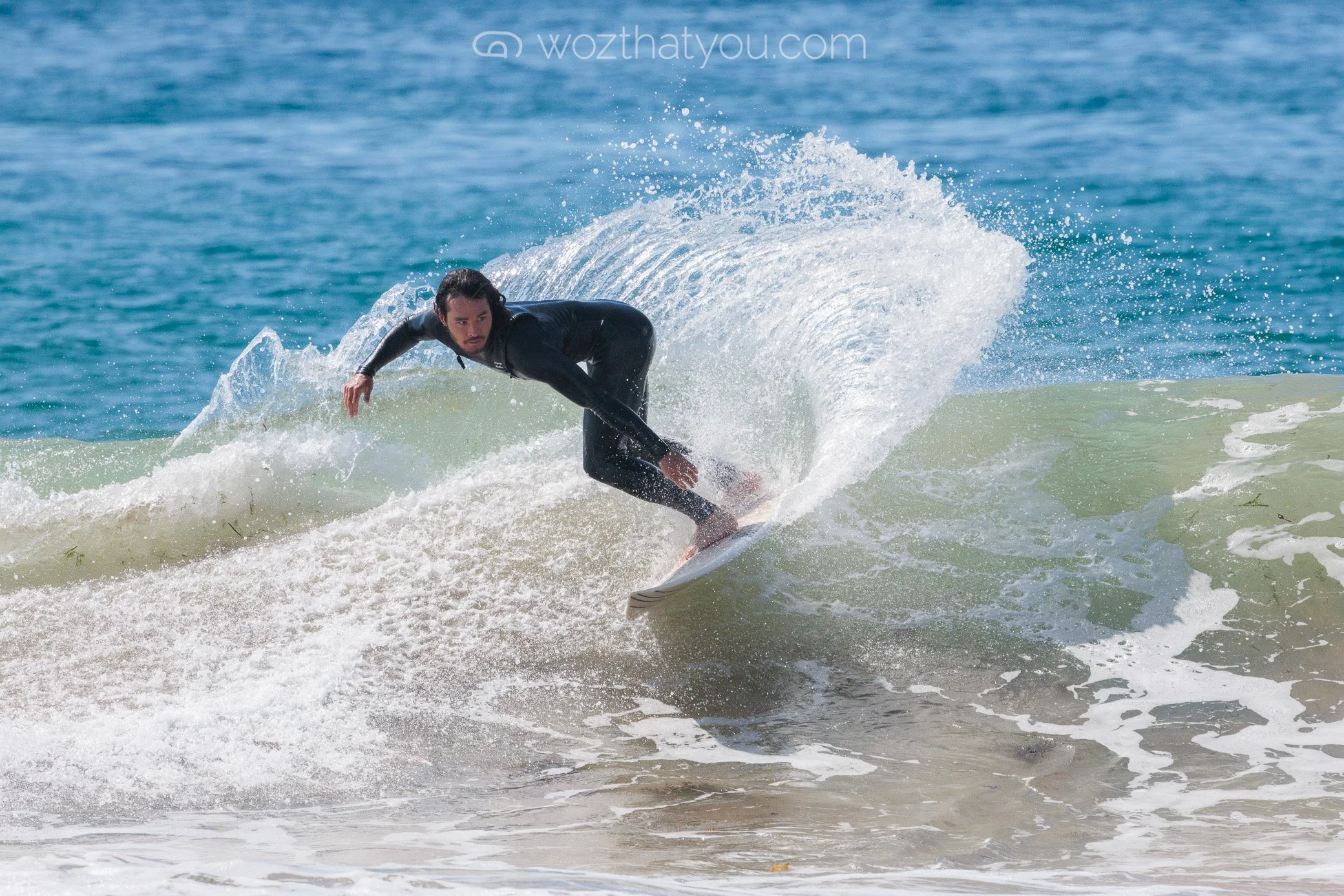 A man in a black wetsuit surfing on a wave in the ocean.