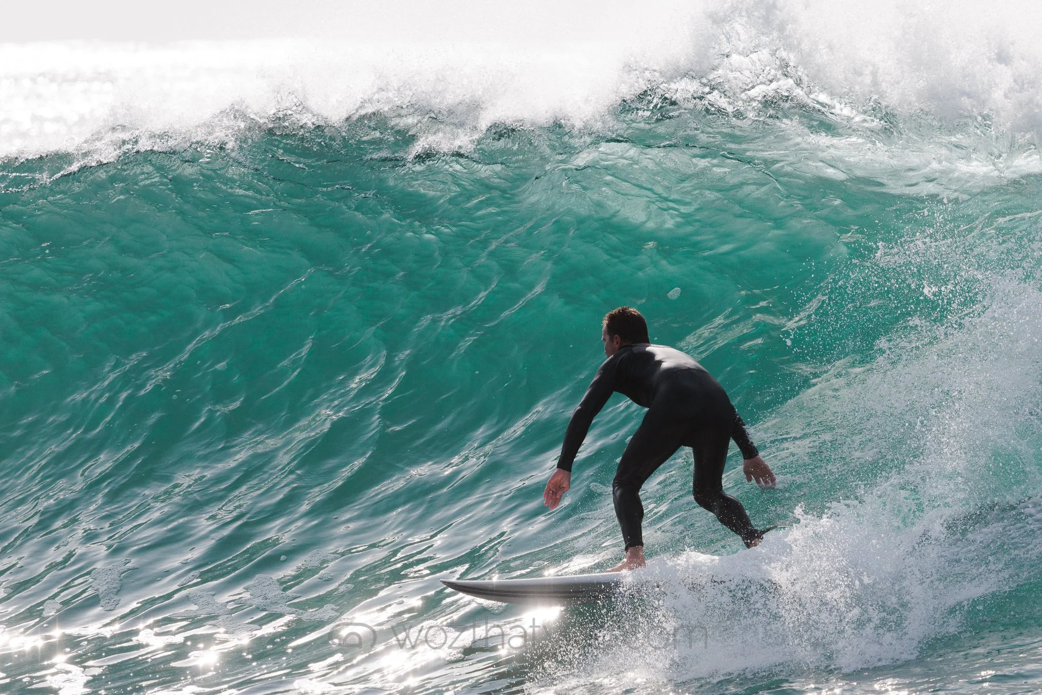 A man in a black wetsuit surfing on a wave in the ocean.