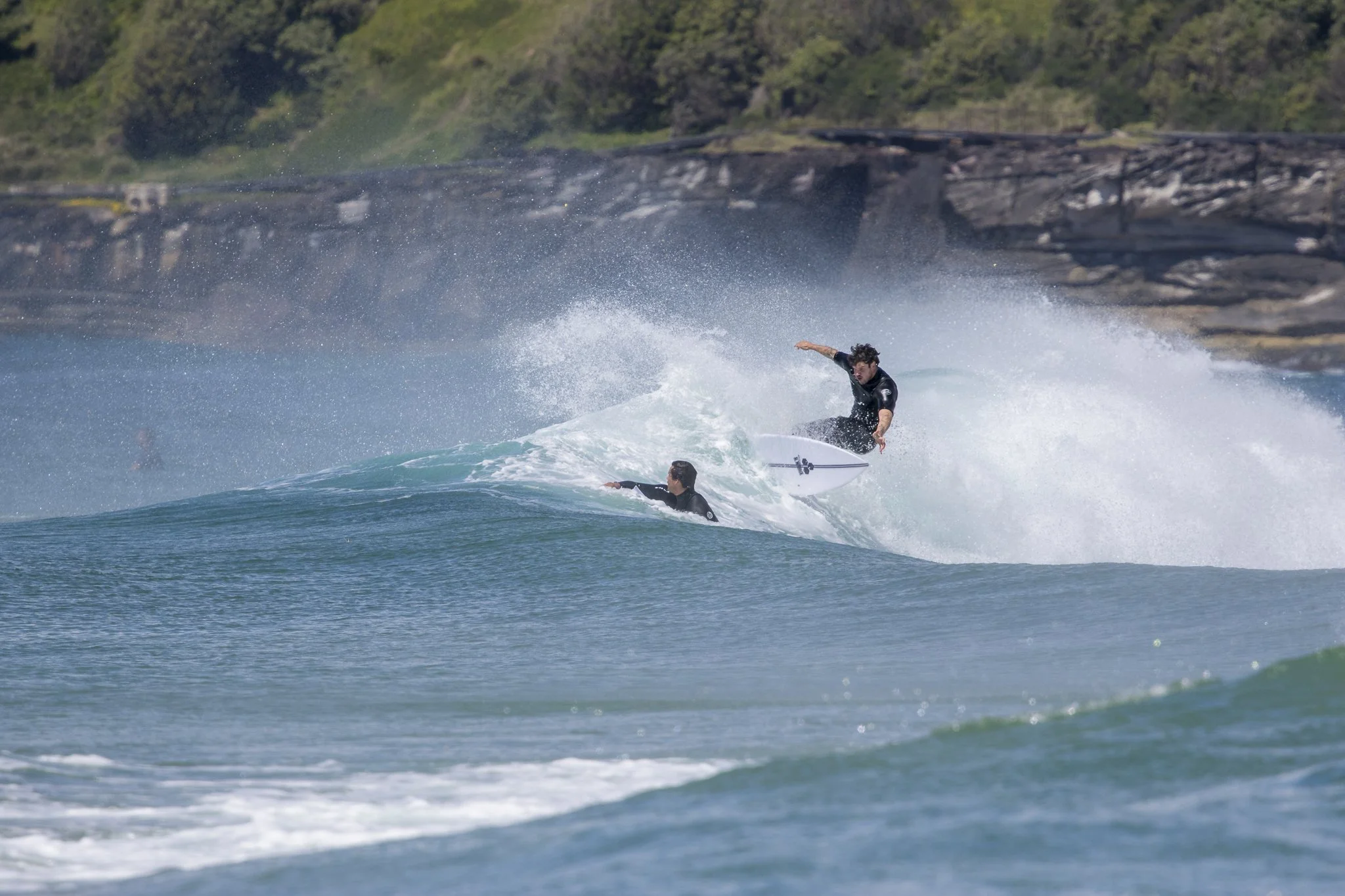 Two surfers riding a wave at the beach, with one surfer executing a maneuver above the other.