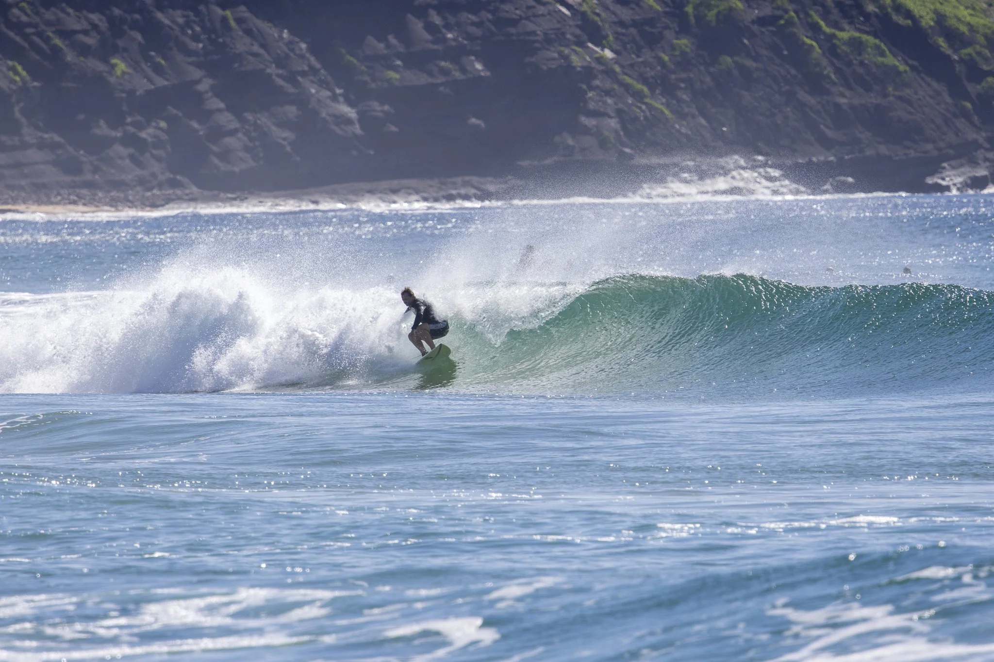 A person surfing on a wave in the ocean with cliffs in the background.