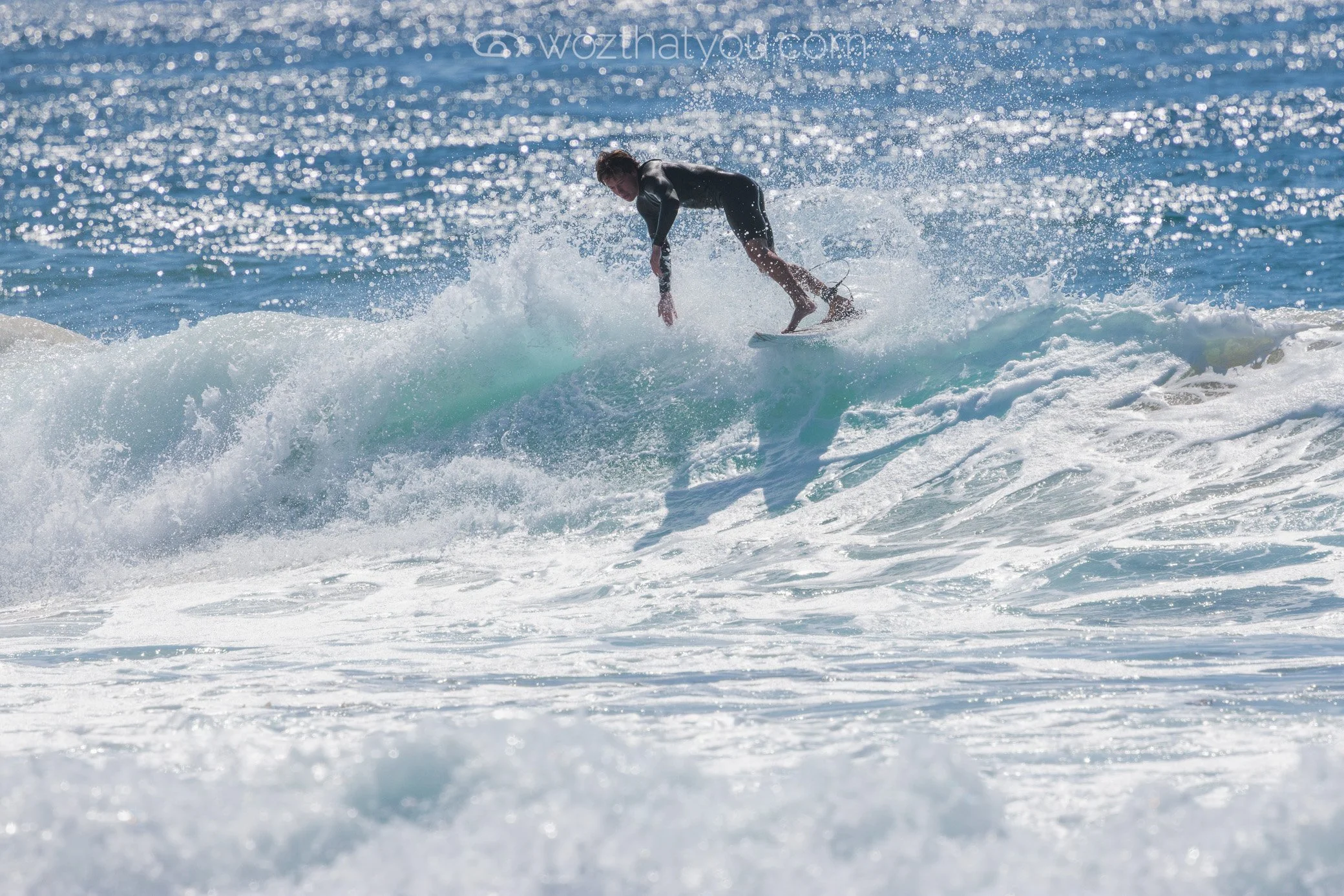Person surfing on a wave in the ocean with sunlight reflecting off the water.