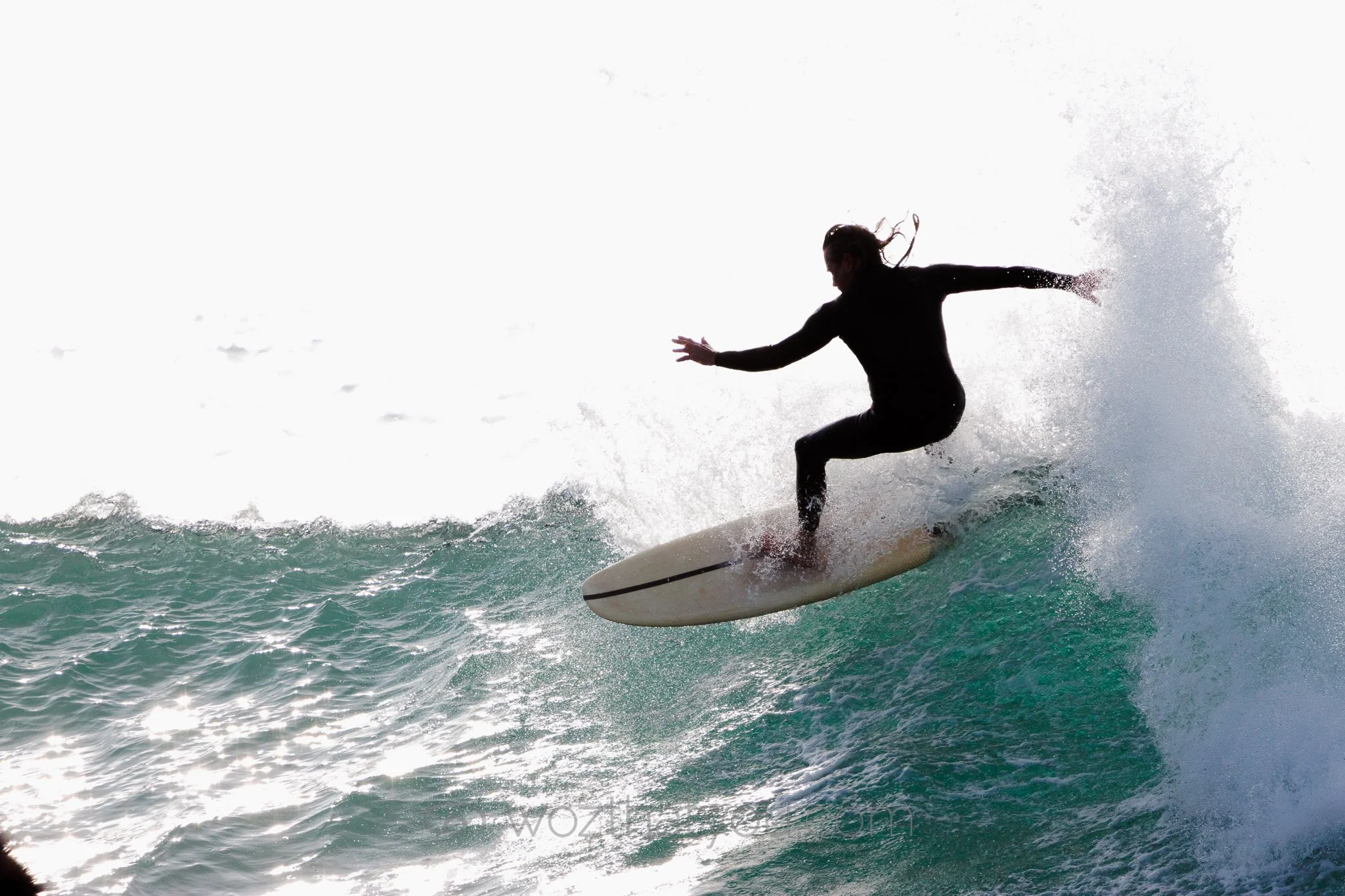 Silhouetted woman surfing on a wave with spray and foam
