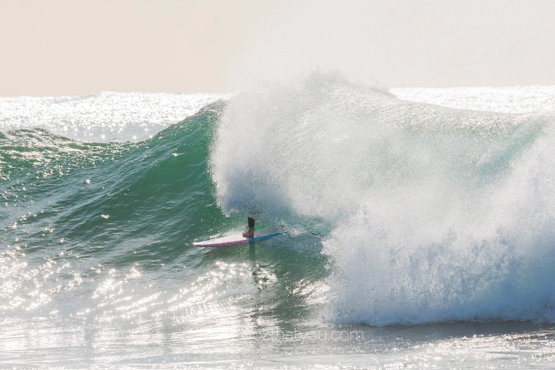 Surfer riding inside a large ocean wave with spray and foam.