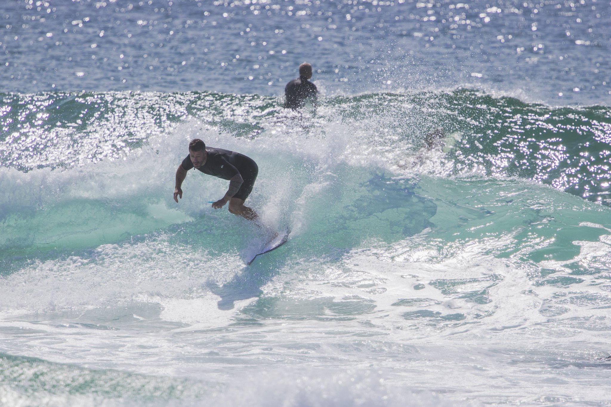A man surfing on a wave with another person in the background in the ocean under a clear sky.