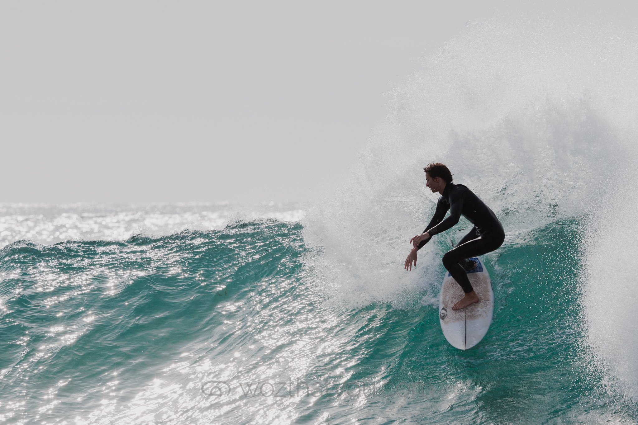 A person surfing on a wave in the ocean wearing a black wetsuit.